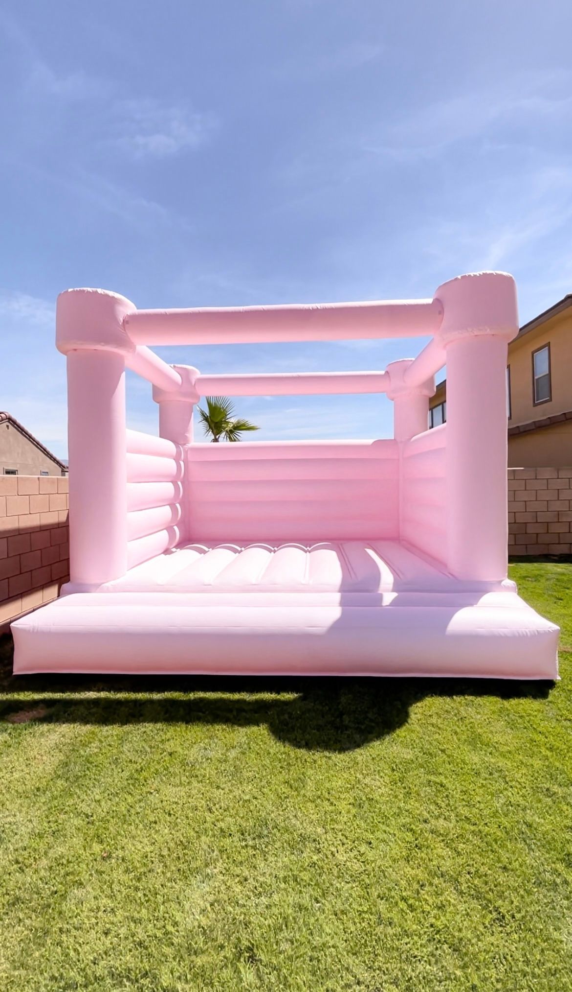 Pink inflatable bounce house on a grassy backyard lawn under a sunny blue sky