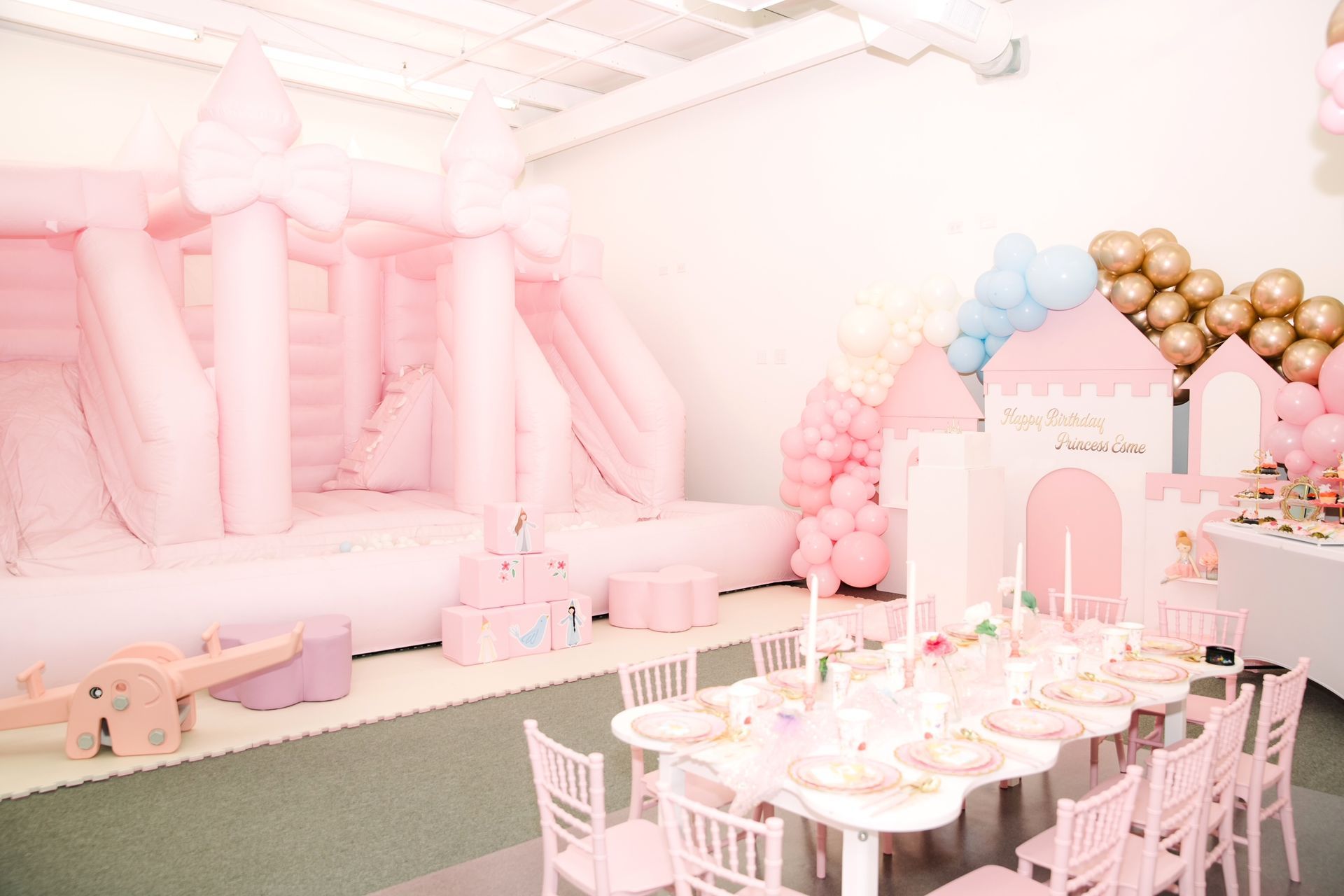Pastel pink party setup with white table settings, balloon garlands, and a decorated dessert display