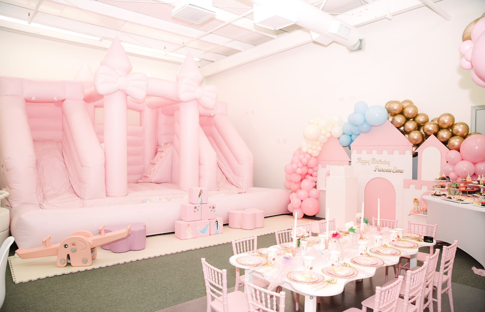 Pastel pink party setup with giant balloon letters, tables, chairs, and balloon decorations in a bright room