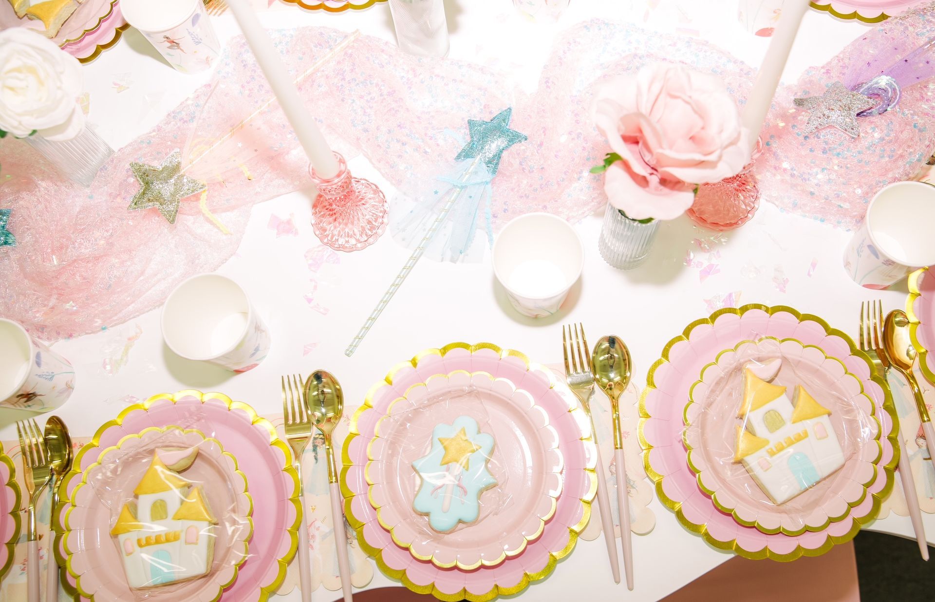 Pastel pink party table with decorated cakes, plates, teacups, and gold utensils