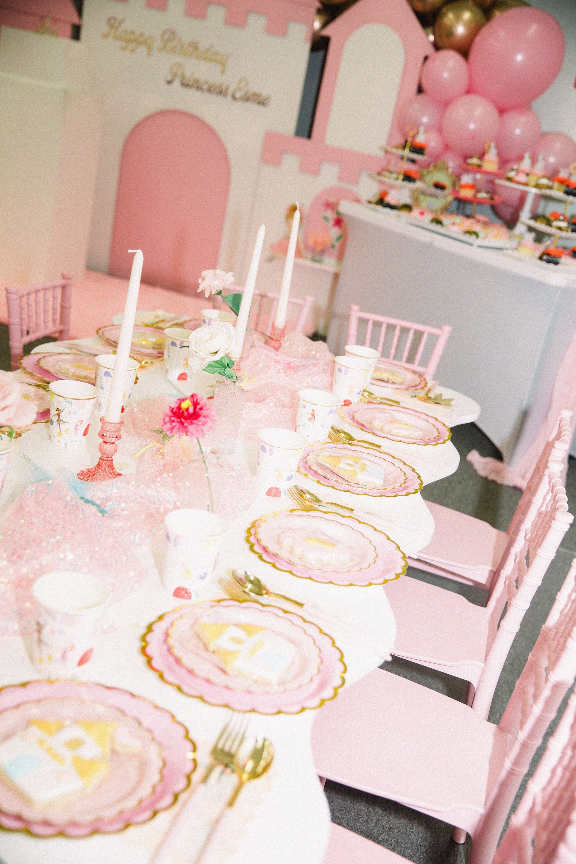Pastel birthday party table with pink balloons, cakes, and decorated plates in a pink room