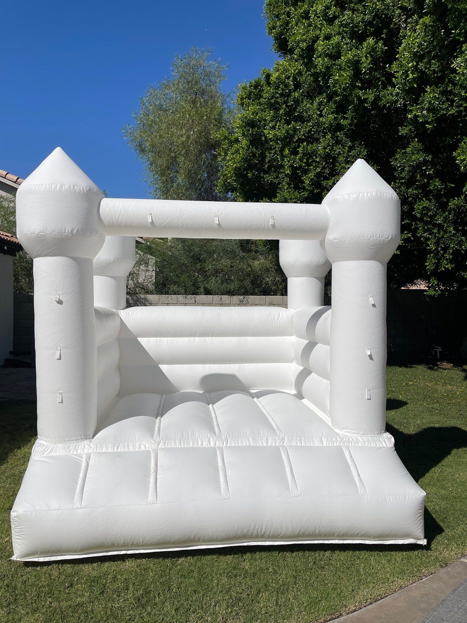 White inflatable bounce house on grass with blue sky and trees in the background