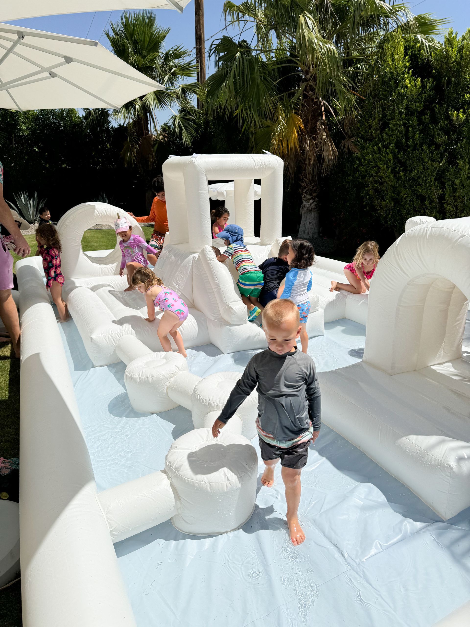 Children playing on a white inflatable water slide in a sunny backyard.