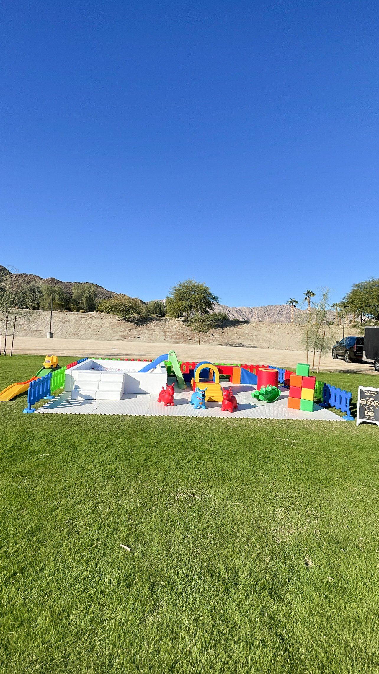Colorful children’s chairs on grass beside a concrete wall under a bright blue sky