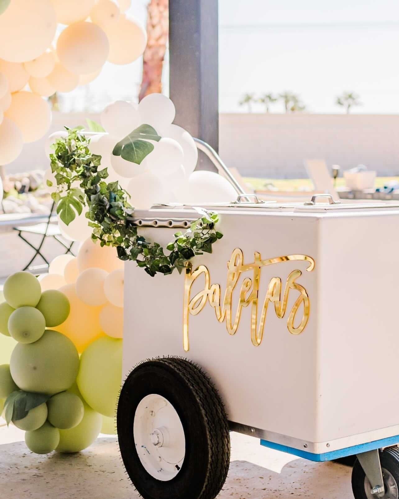 White party cart with gold “Patis” sign, greenery, and pastel balloons at a bright celebration