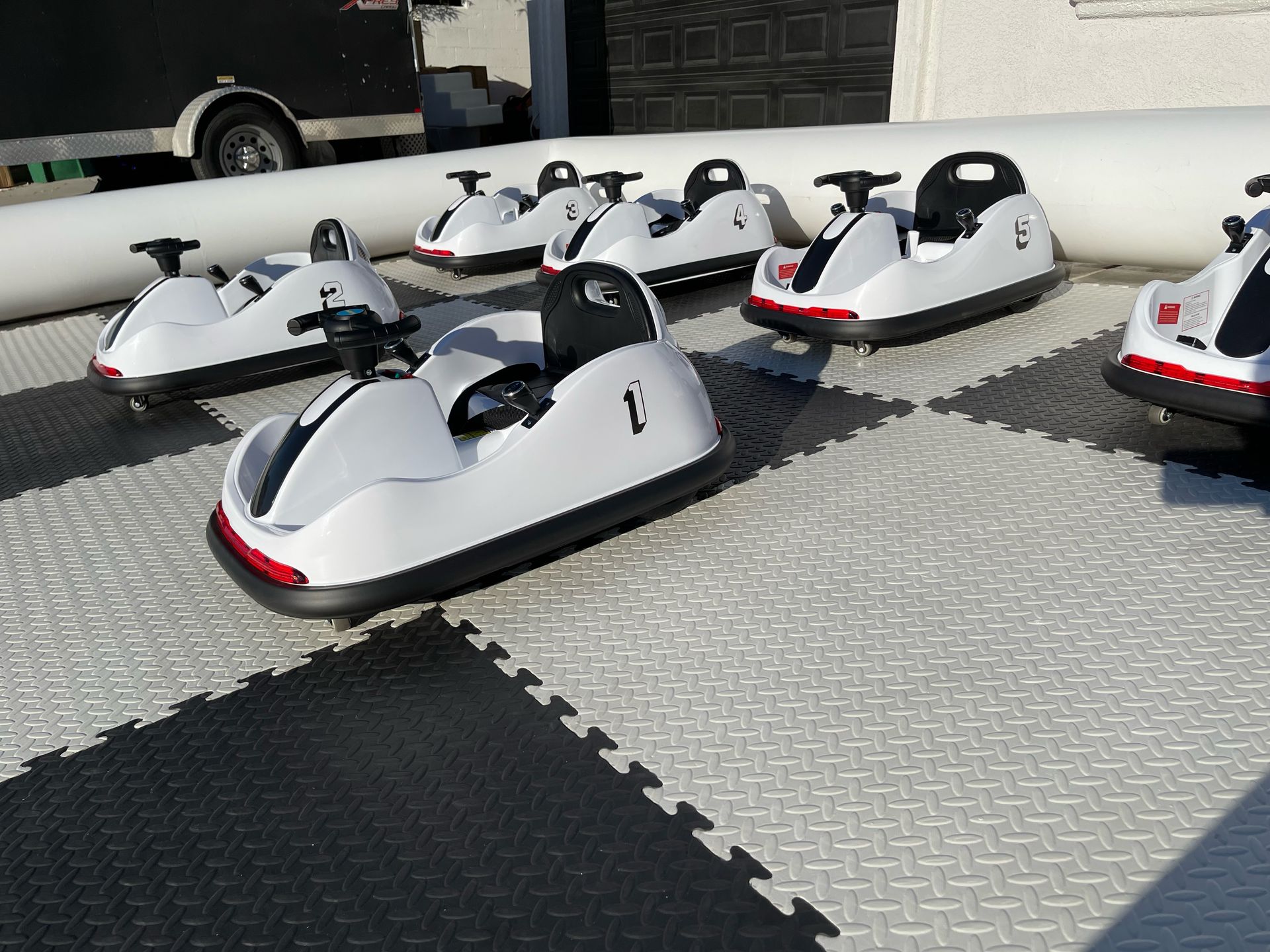 Row of white bumper cars with black seats parked on a paved lot in sunlight