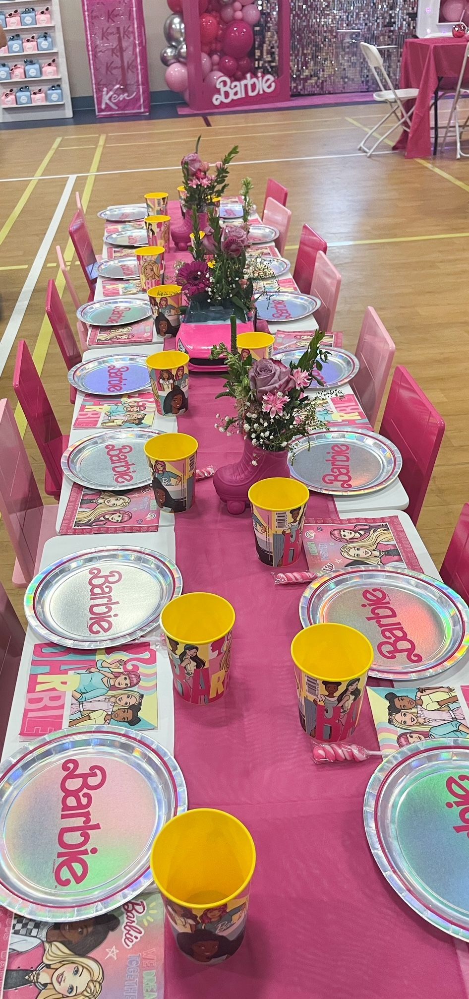 Pink birthday party table set with plates, cups, candles, and a floral centerpiece on a decorated floor