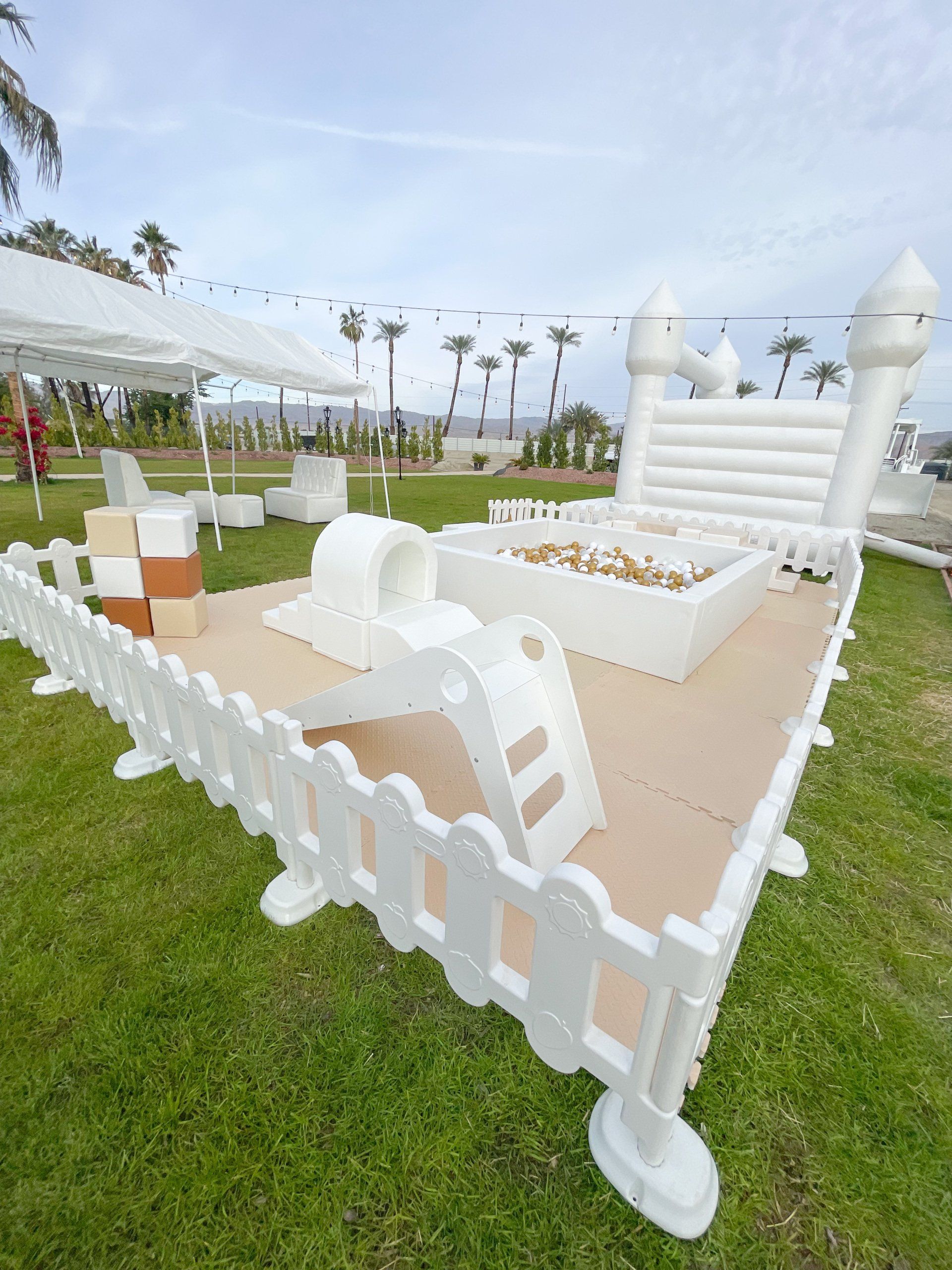 White fenced outdoor play area with slides and toy blocks on grass under a cloudy sky