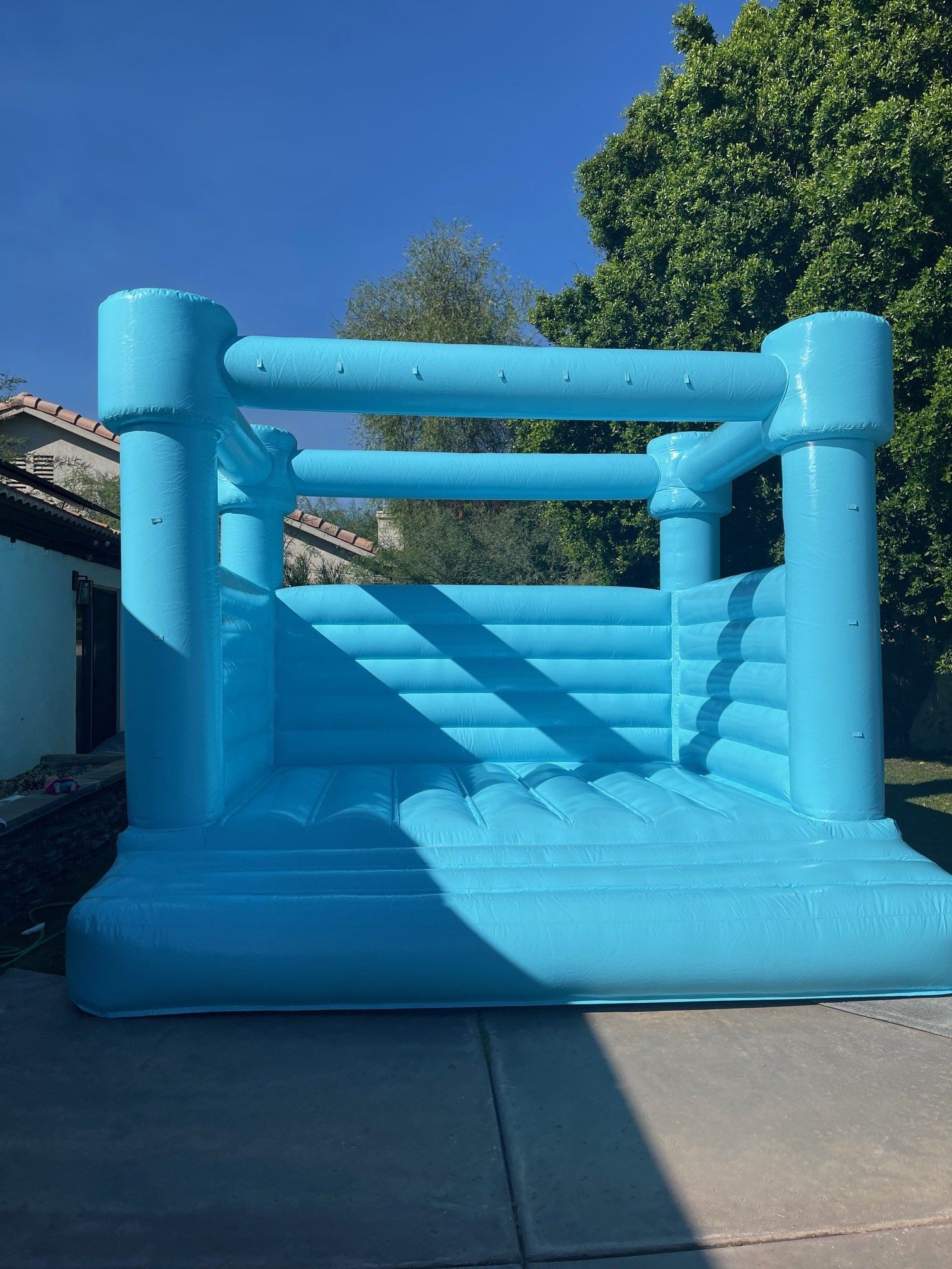 Bright blue inflatable bounce house outdoors in a sunny yard, with a clear blue sky behind it