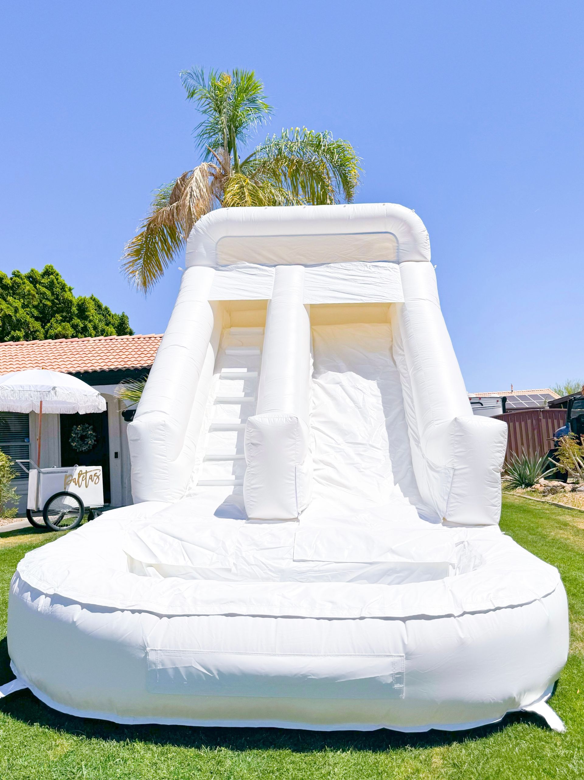 White inflatable slide with steps and a round base on a lawn under a blue sky.