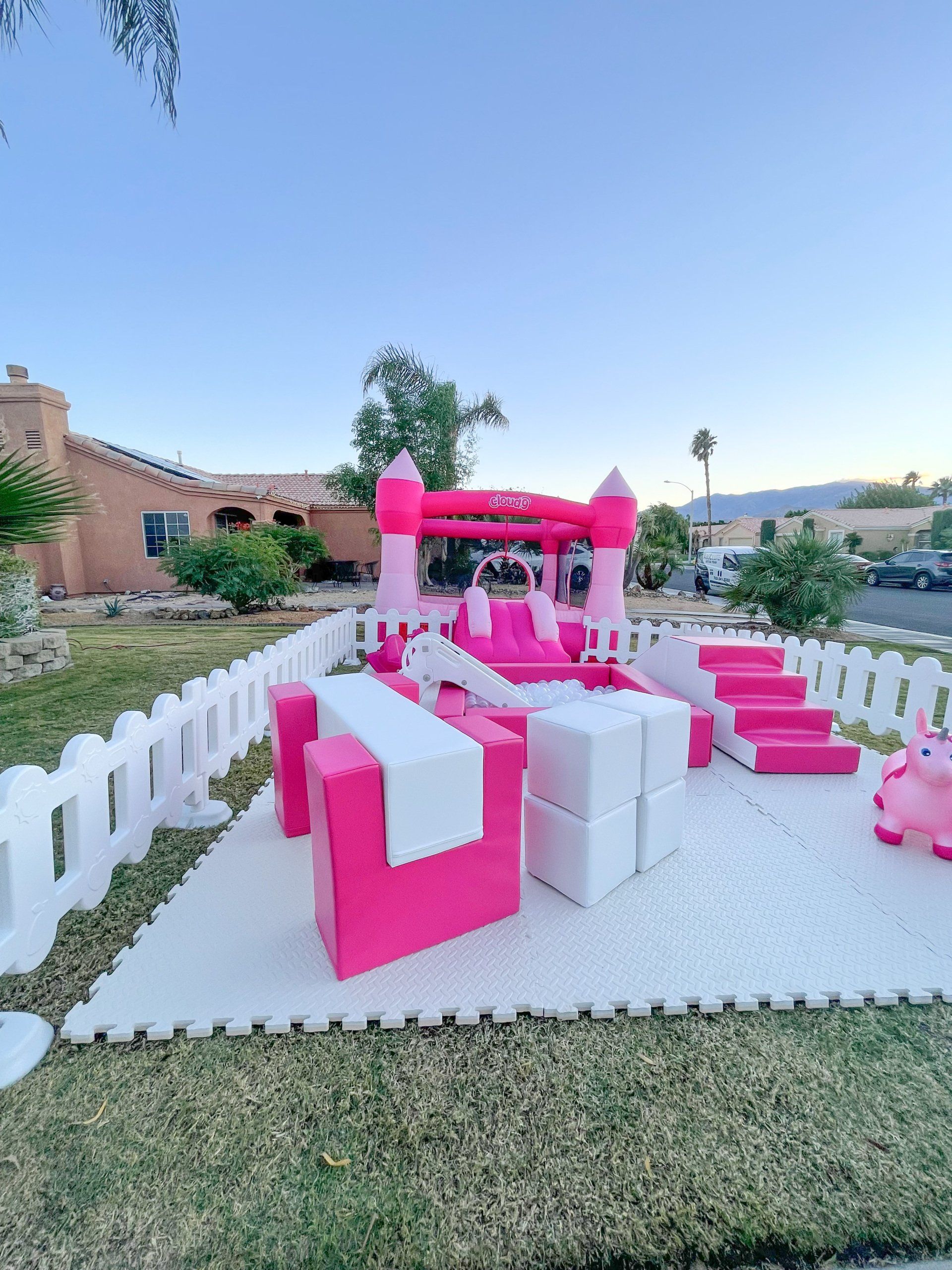 Pink-and-white outdoor party seating under a canopy on a lawn, with a castle-like building in the background
