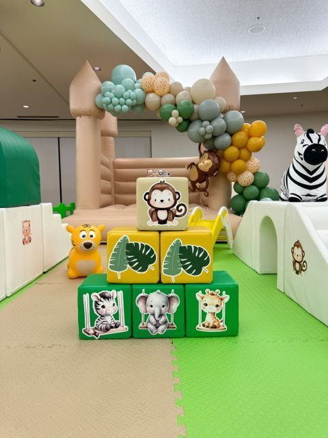 Balloon arch over a kids’ play area with cartoon animal blocks and toy figures on a green mat