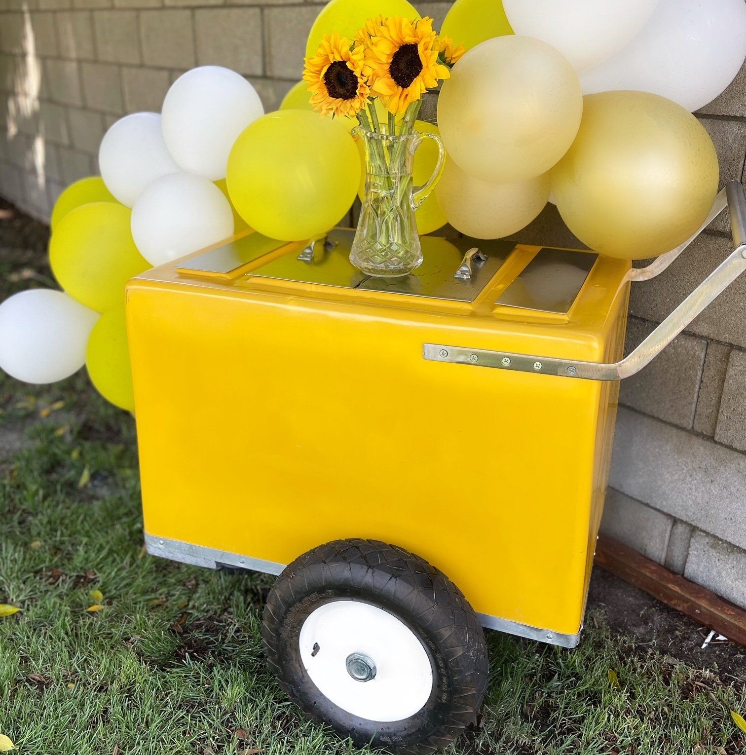 Yellow cart decorated with white and yellow balloons and sunflowers on a porch