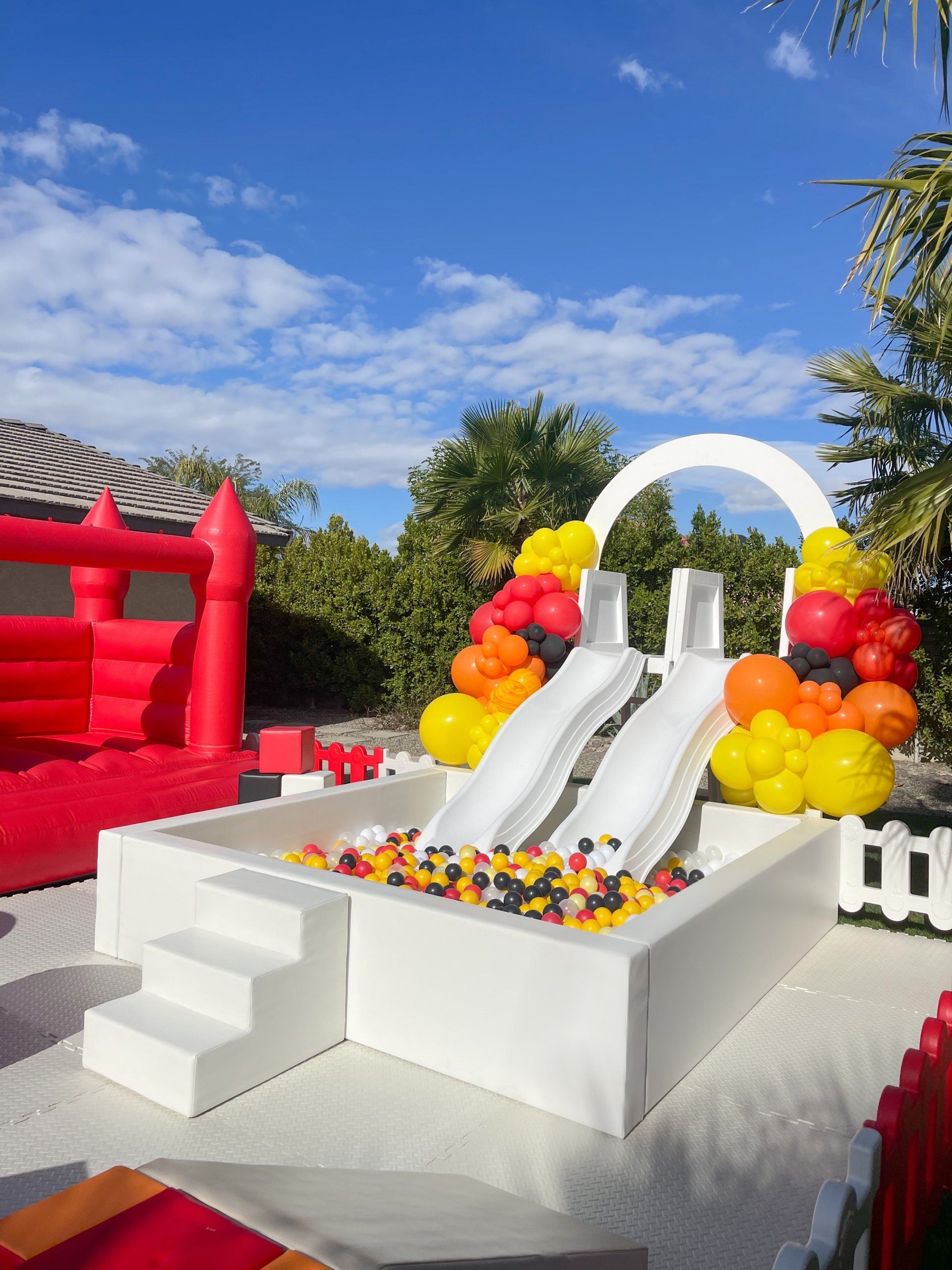 White twin slide on a decorated outdoor party setup with balloons and a red inflatable bounce house