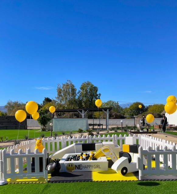White fenced lawn display with yellow balloons and a yellow-and-white vehicle under a clear blue sky