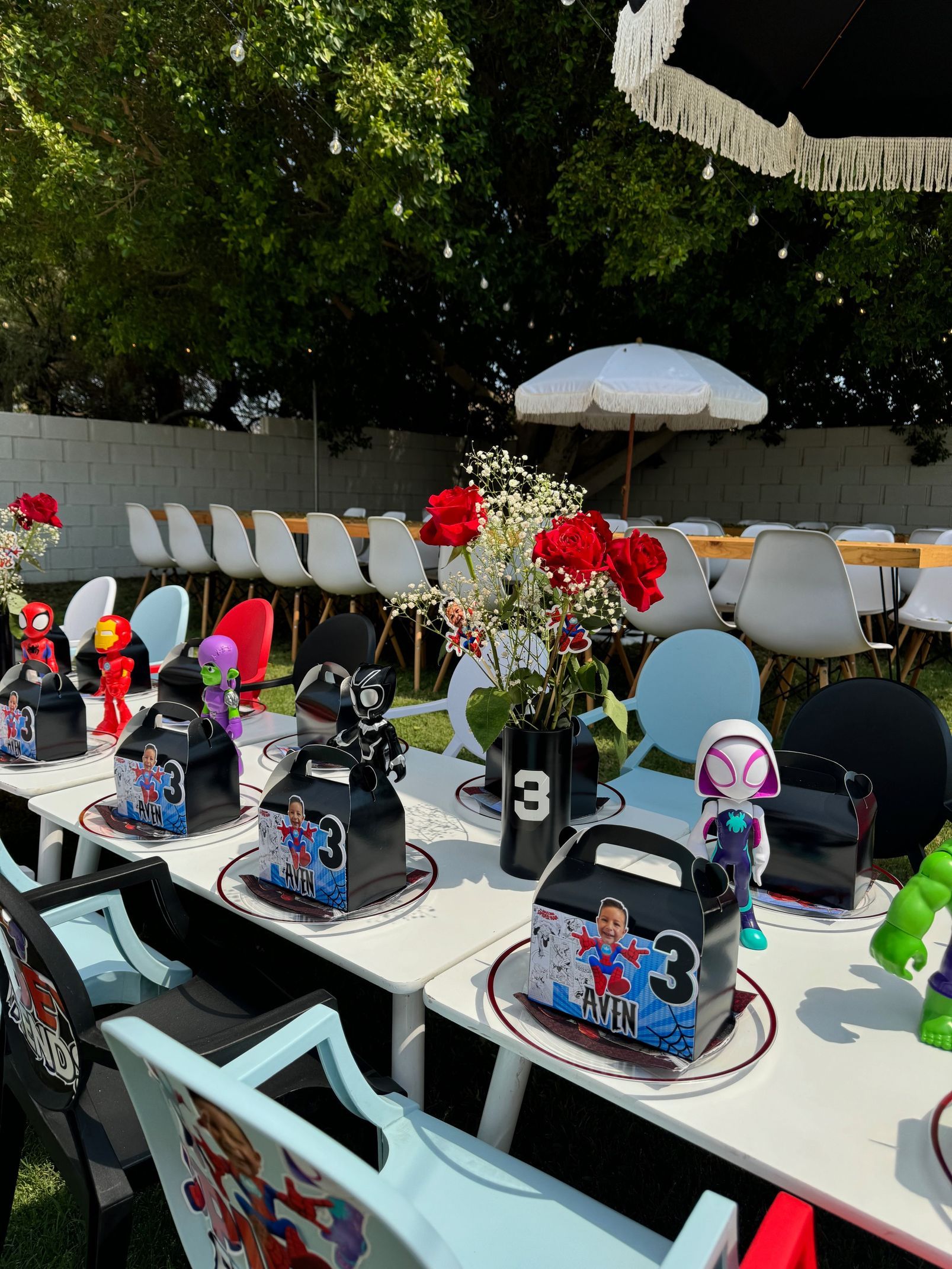 Outdoor cafe table set with colorful mugs, flowers, and numbered signs under trees