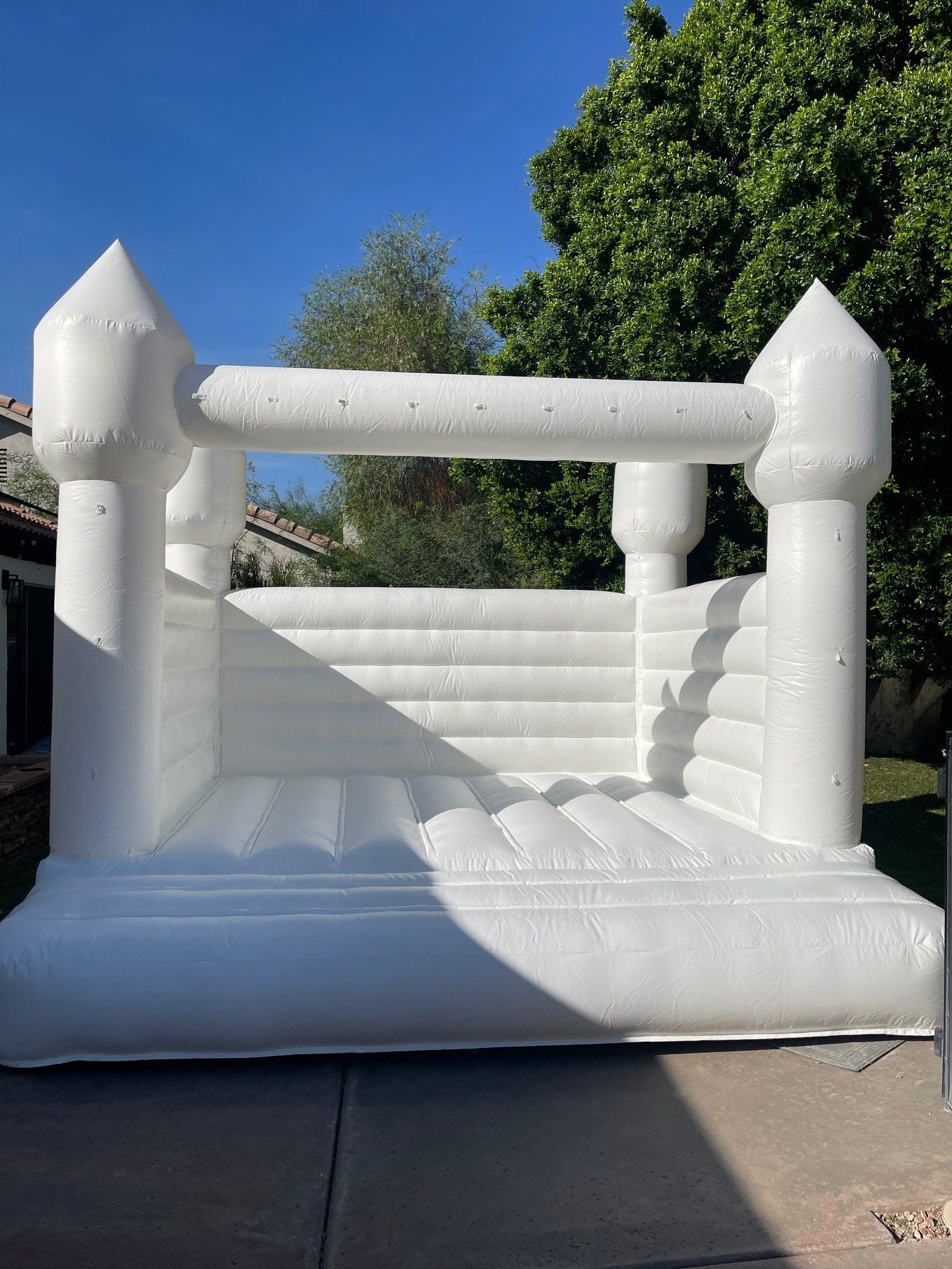 White inflatable castle bounce house with towers on a driveway in bright sunlight.