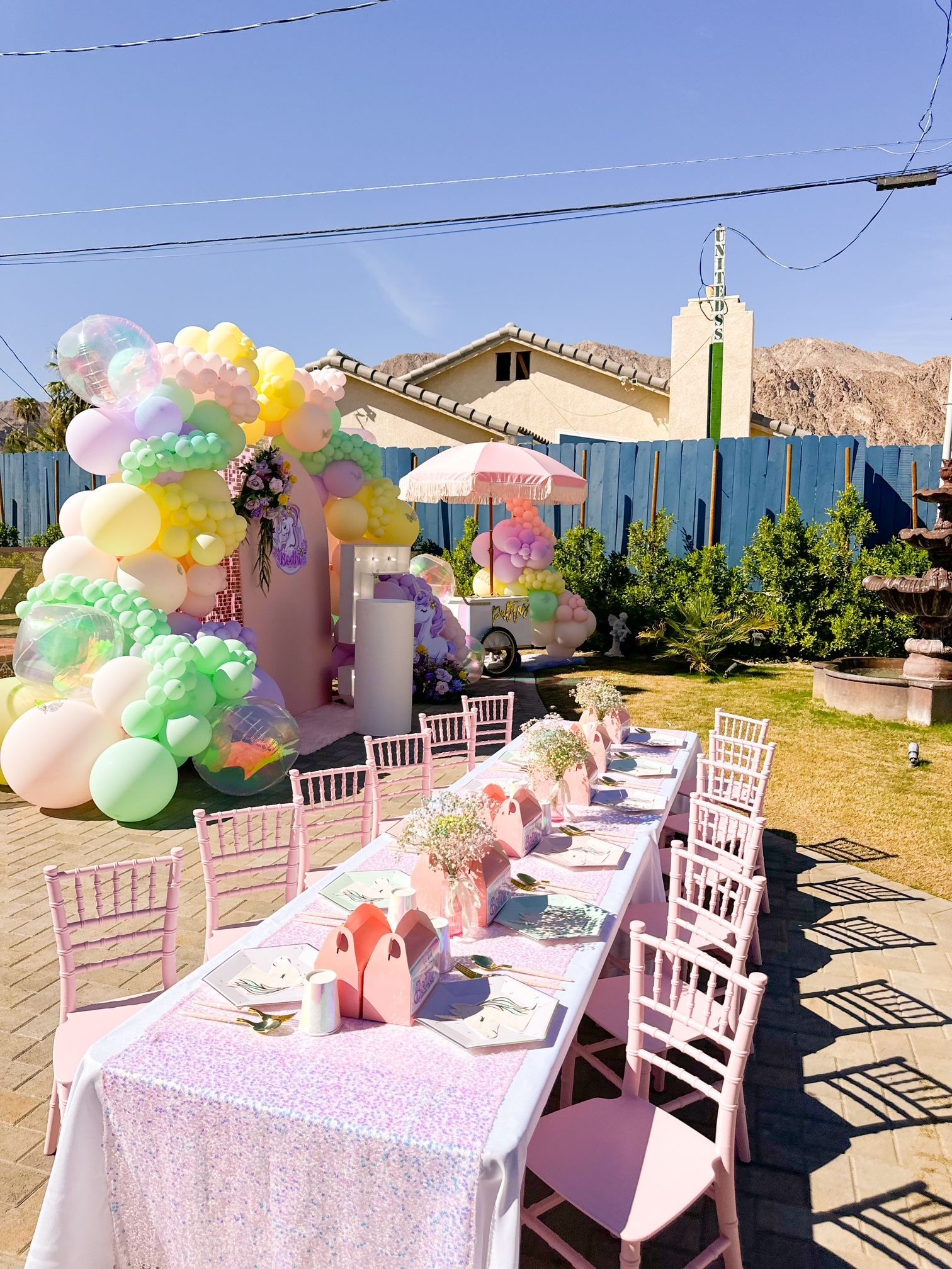 Pastel balloon arch beside a decorated outdoor dining table in a sunny backyard garden