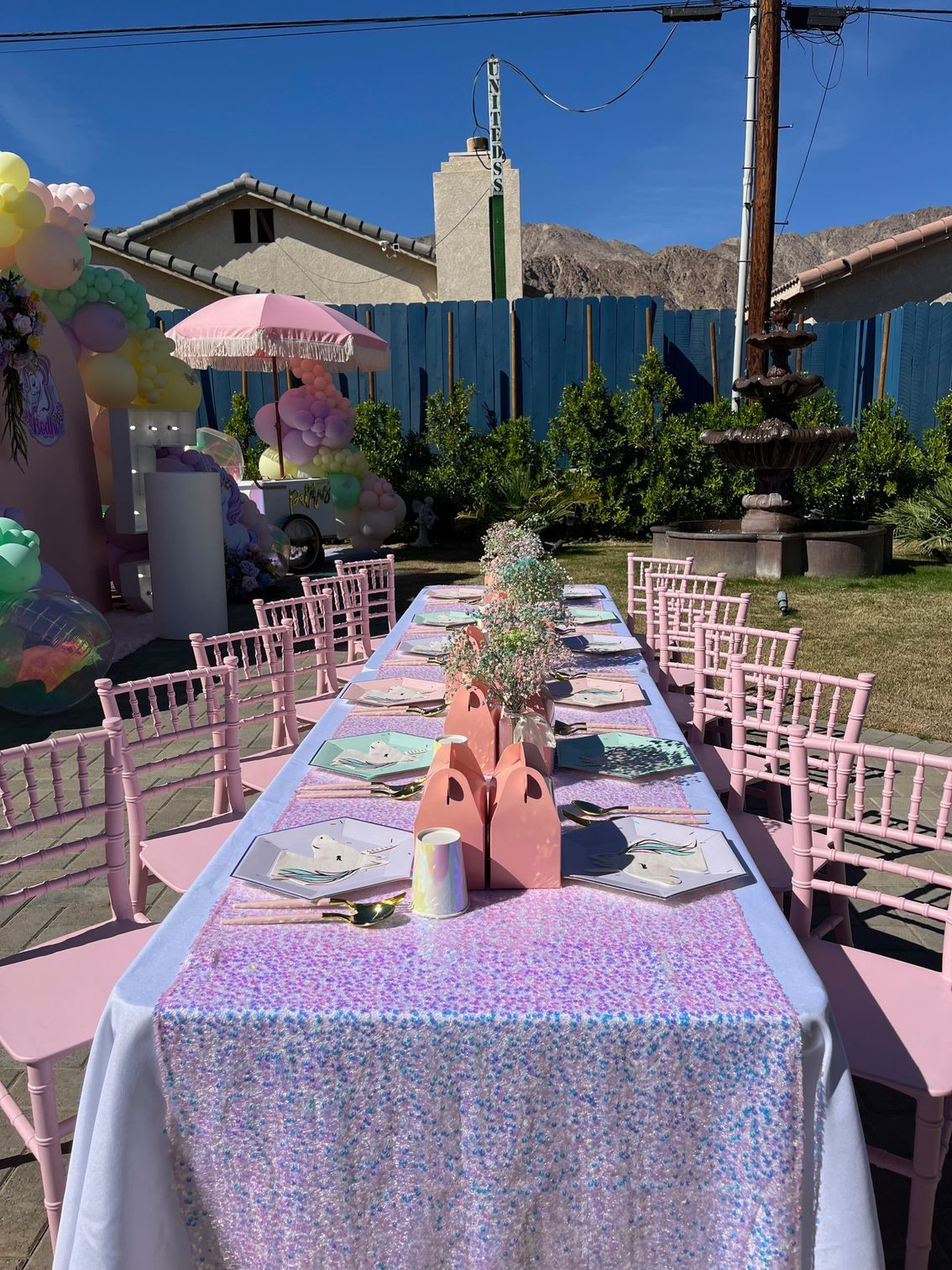 Long pink outdoor party table set with floral decor in a sunny backyard garden