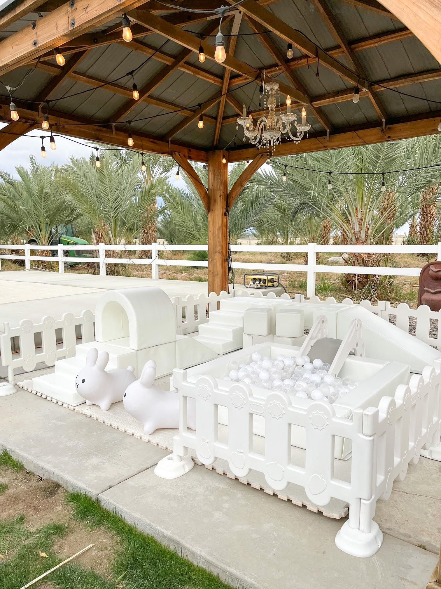 White outdoor playpen with toys under a wooden pavilion on a concrete patio