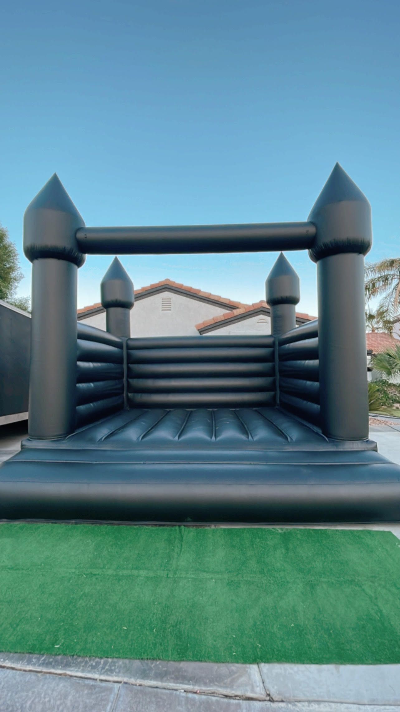 Black inflatable bounce house with green base in a backyard under a blue sky