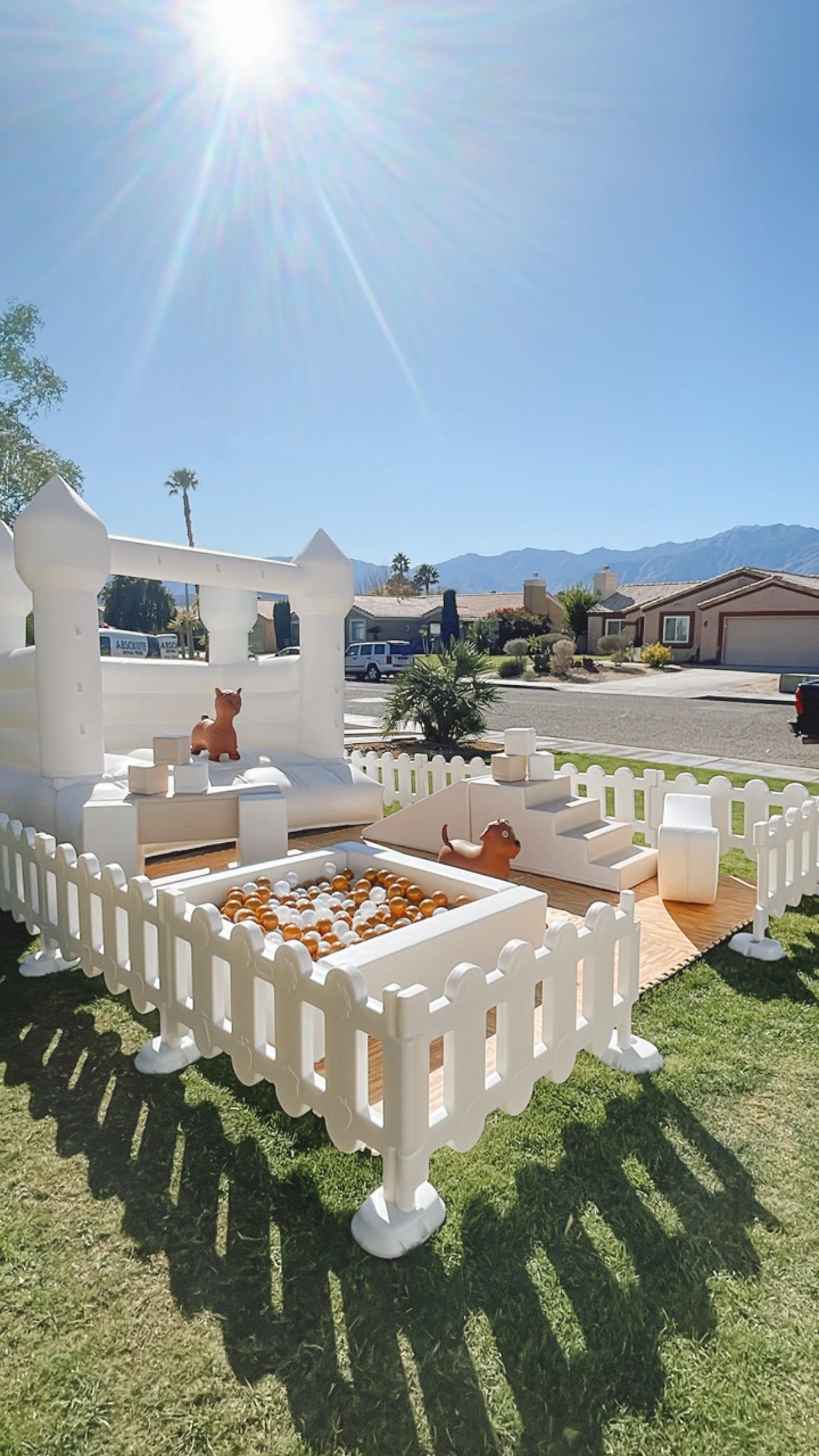 Sunlit cemetery plot with white picket fence, flower arrangements, and memorial markers under a bright blue sky