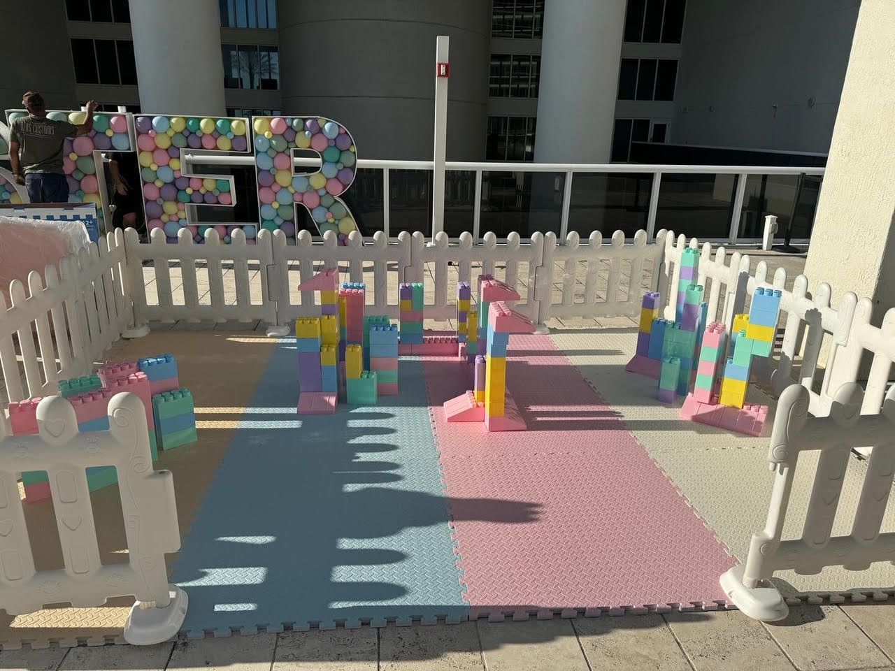 Colorful block play area on foam mats inside a fenced outdoor courtyard.