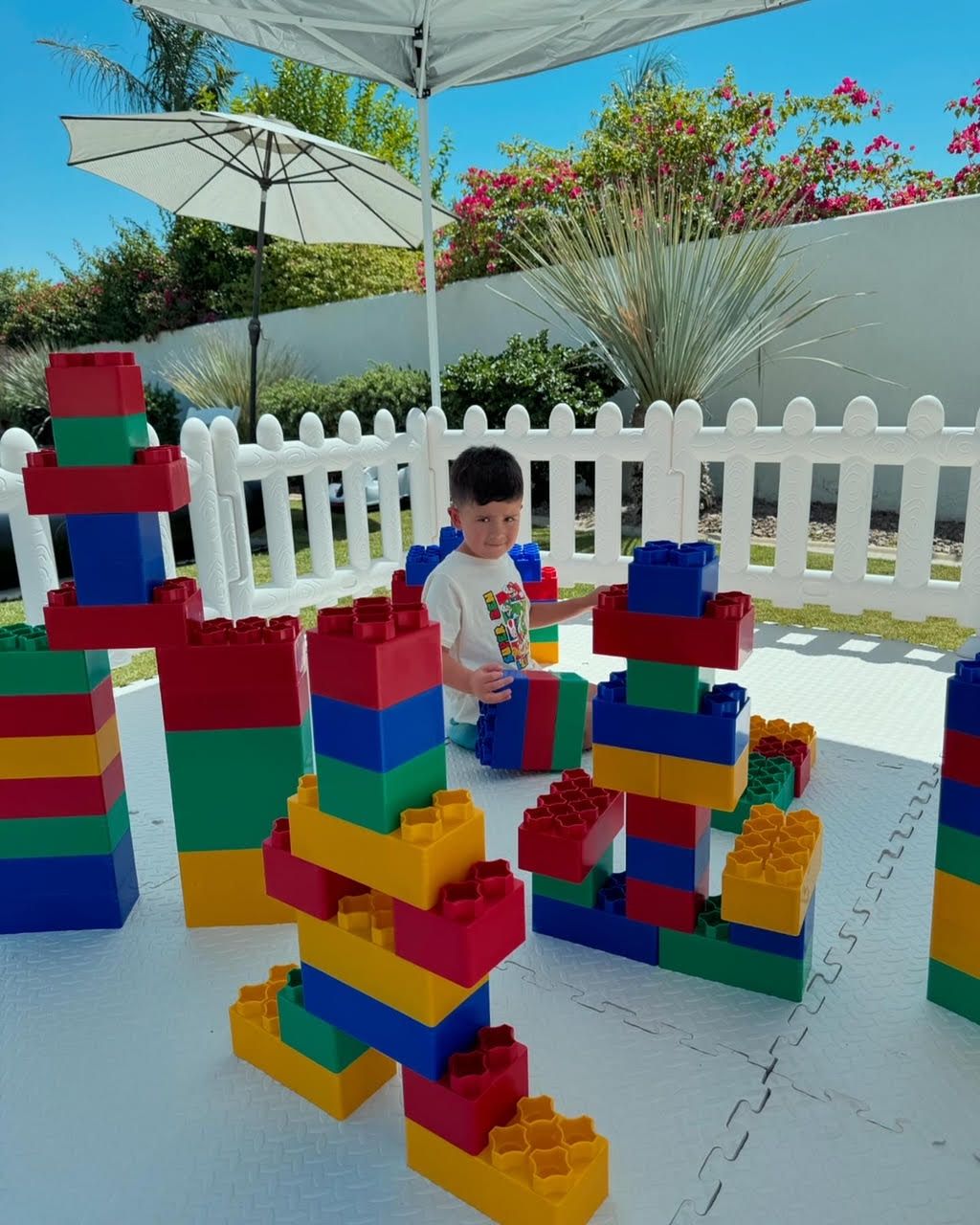 Child building colorful block towers outdoors on a sunny patio with white fence and umbrellas