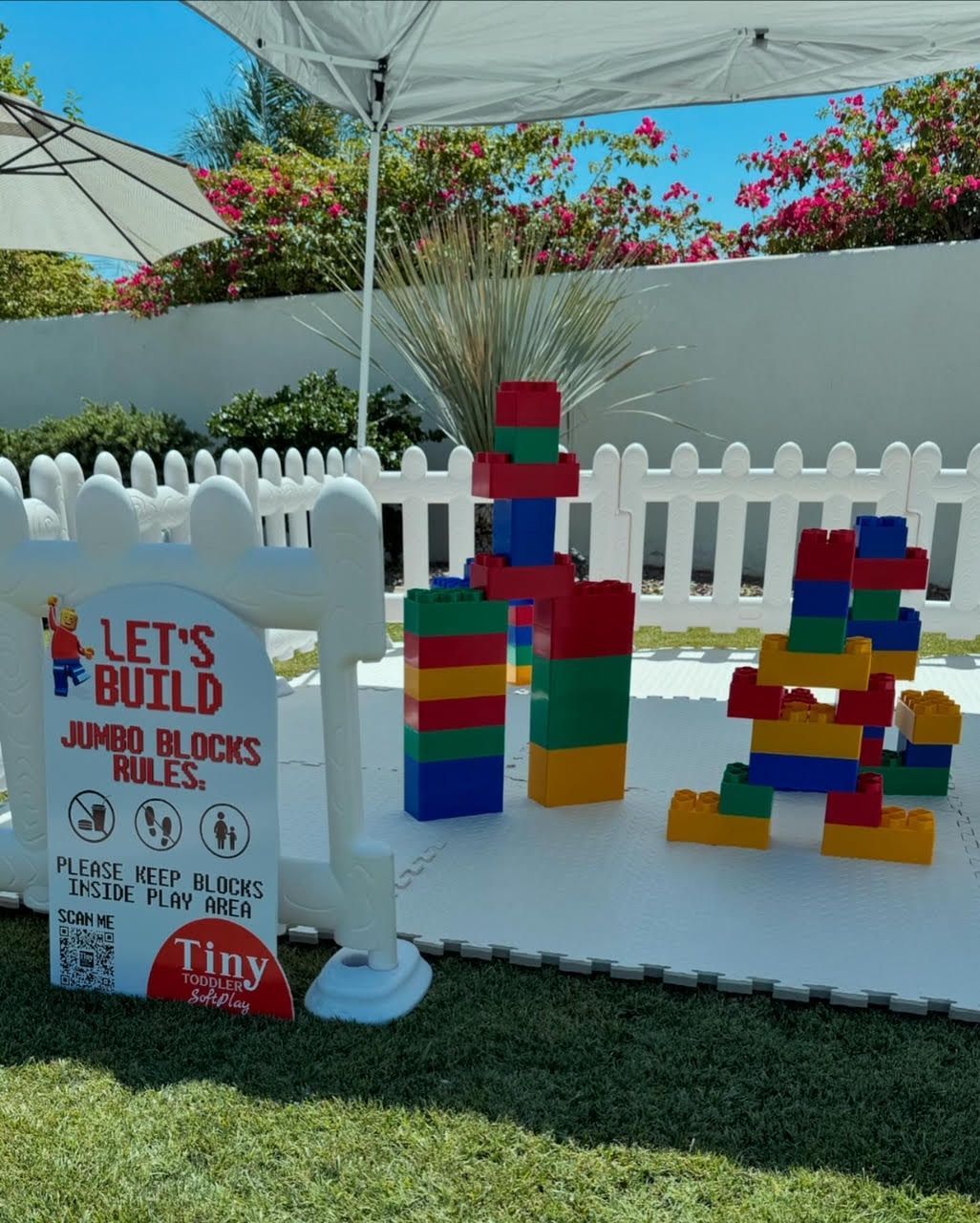 Colorful giant blocks stacked under a canopy beside a sign reading “Let’s Build Jumbo Blocks”