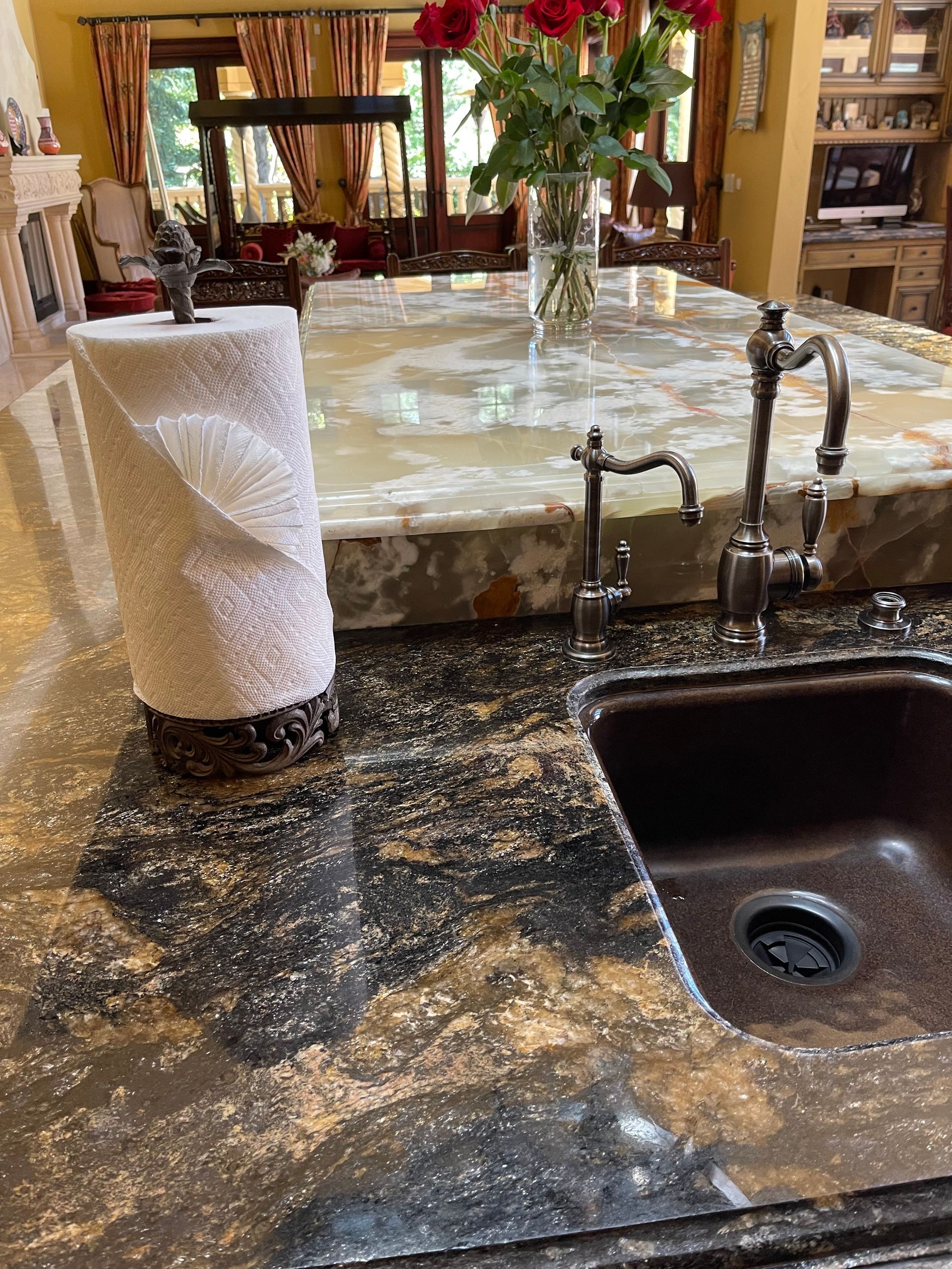 A kitchen sink with a dark basin, granite countertop, paper towel holder, and a small faucet beside a raised stone bar.