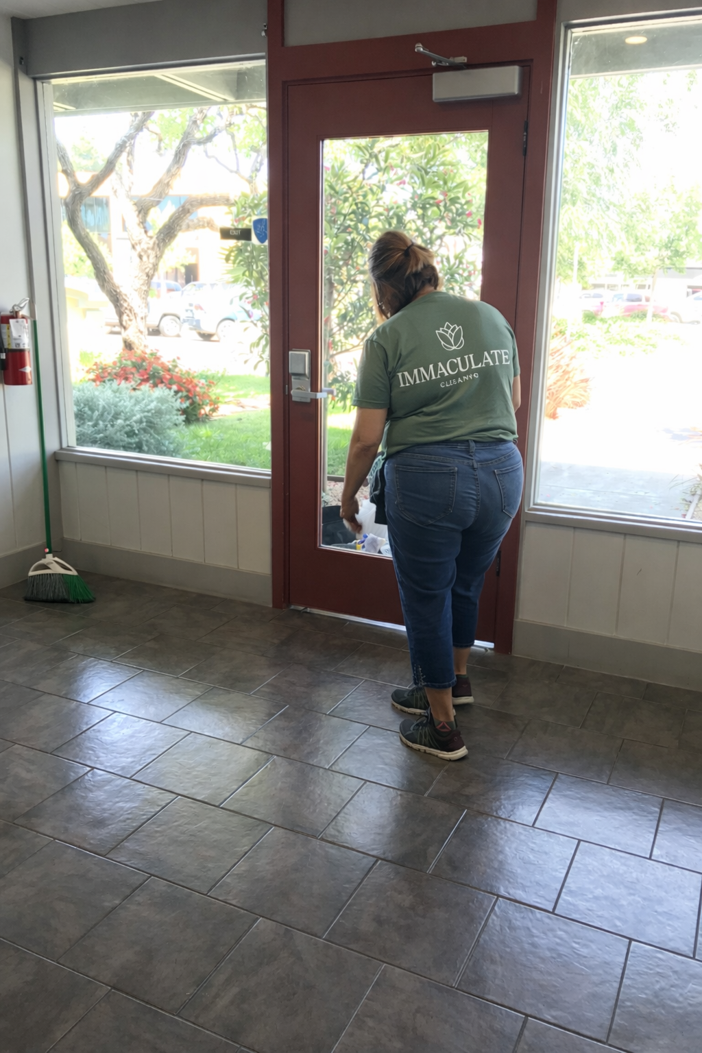 Person in a green shirt opening a glass door in a tiled entryway.