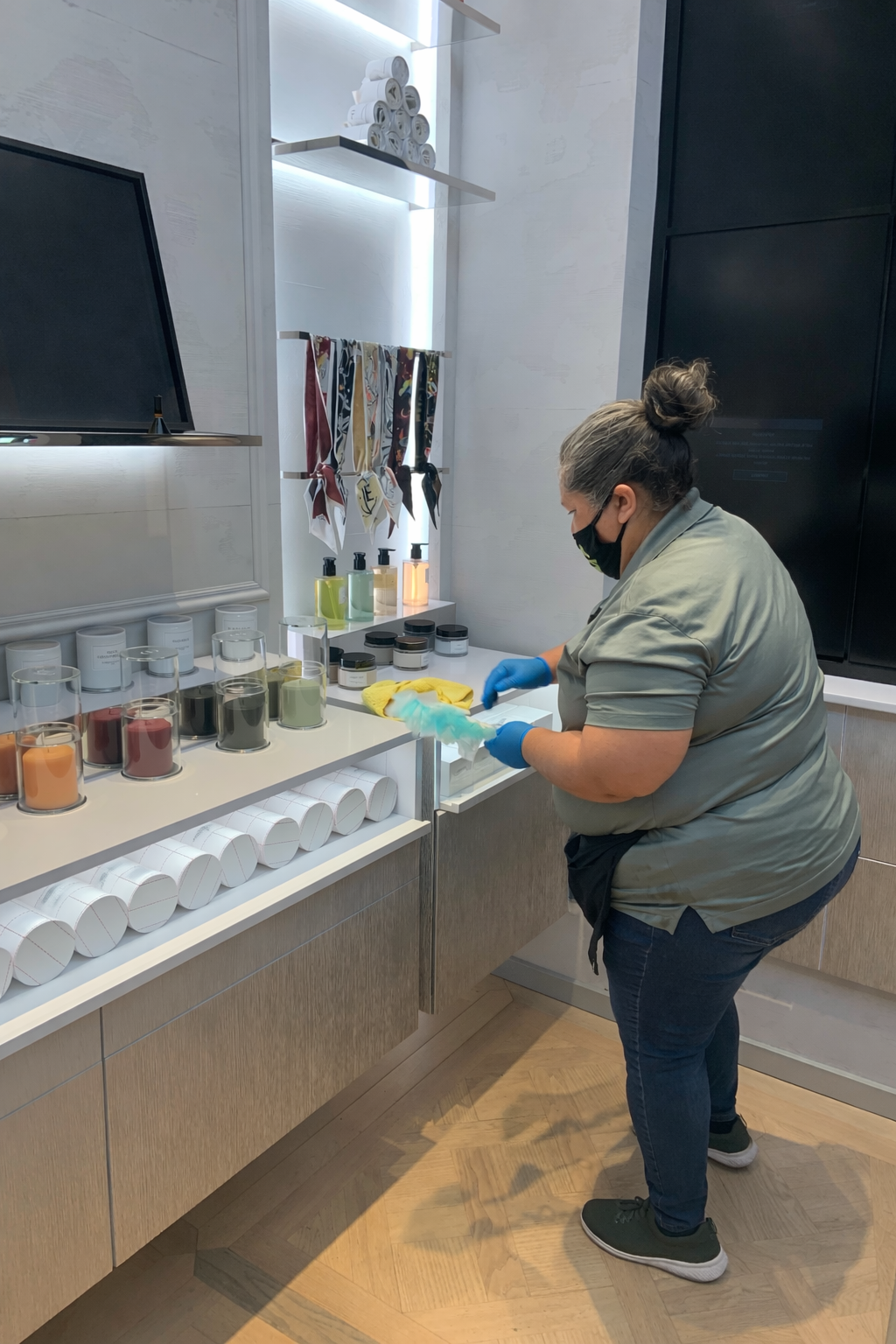 Person in a kitchen washing dishes at a sink, wearing gloves and a mask.