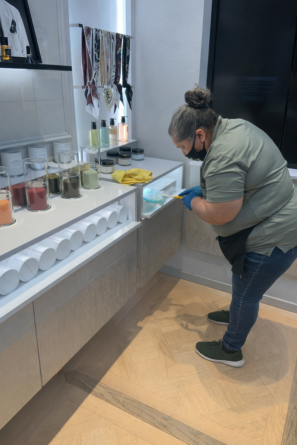 Person bending over a counter in a bright kitchen, looking into a lower cabinet drawer.
