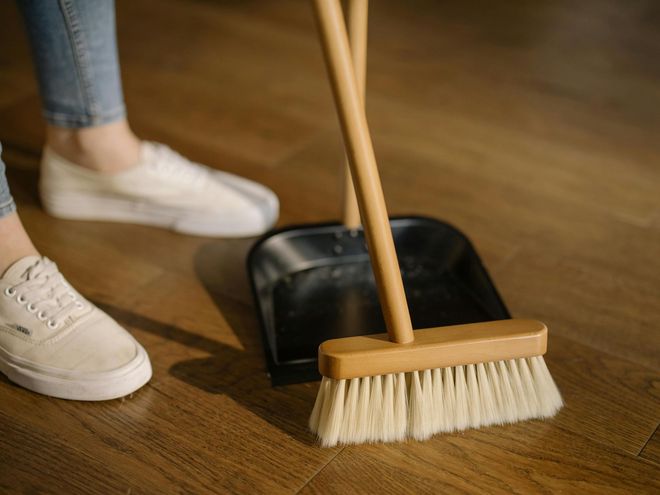 A close-up of a person using a wooden broom to sweep dust. A close-up of a person using a wooden broom to sweep dust.
