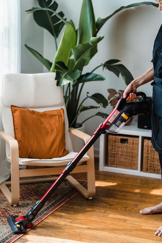 A person uses a red and black cordless stick vacuum.