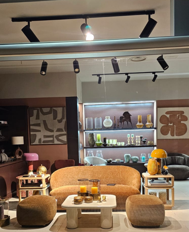 Soggiorno moderno con divano color cuoio, sgabelli rotondi, tavolino da caffè, quadri alle pareti e mensole espositive sotto faretti a binario.