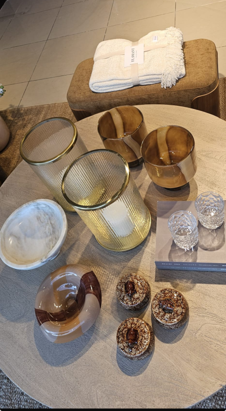 Su un tavolo rotondo sono disposti diversi portacandele decorativi in vetro e ottone, con asciugamani piegati sullo sfondo.