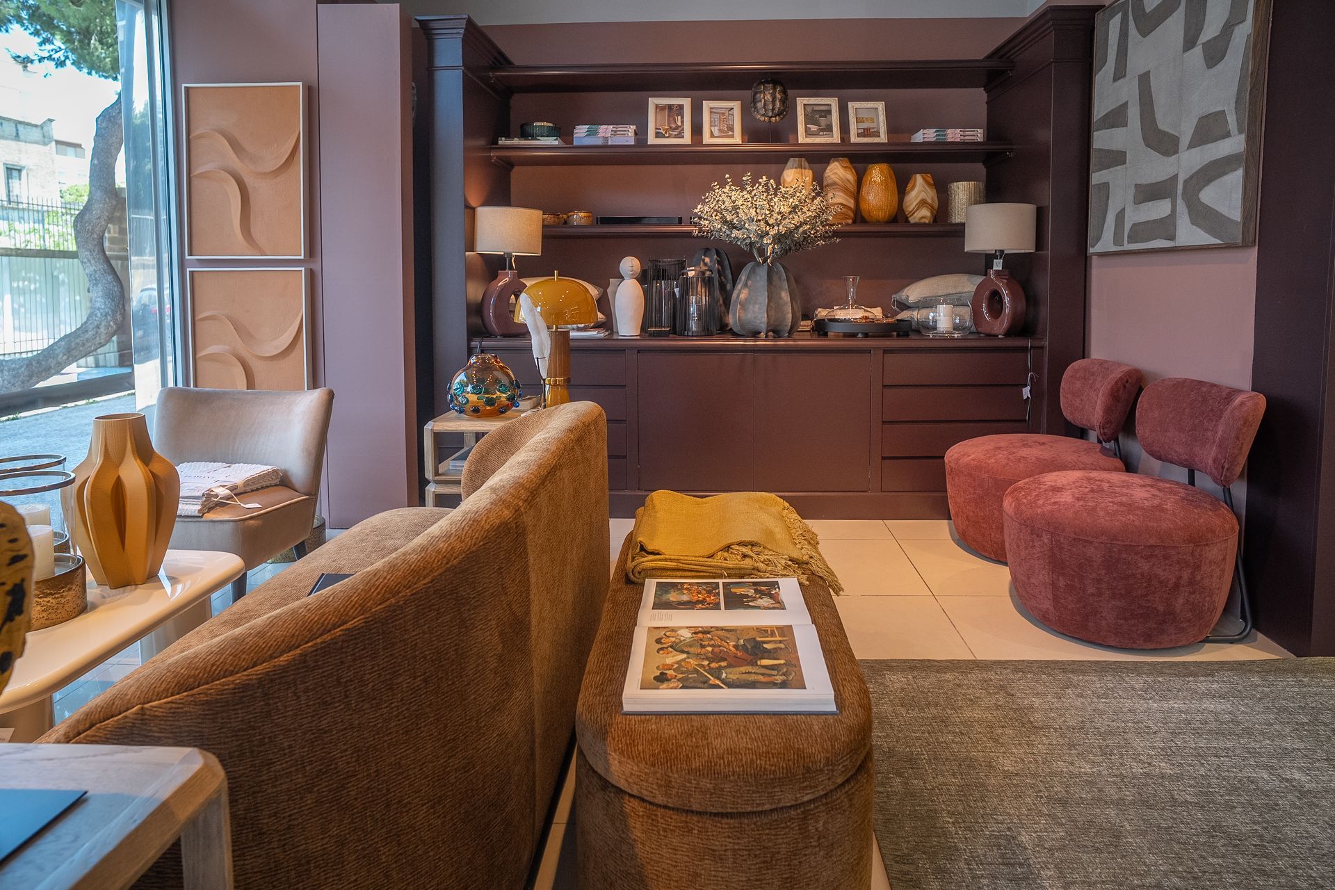 Soggiorno moderno con divano marrone, sedie viola e un mobile in legno scuro con oggetti decorativi.
