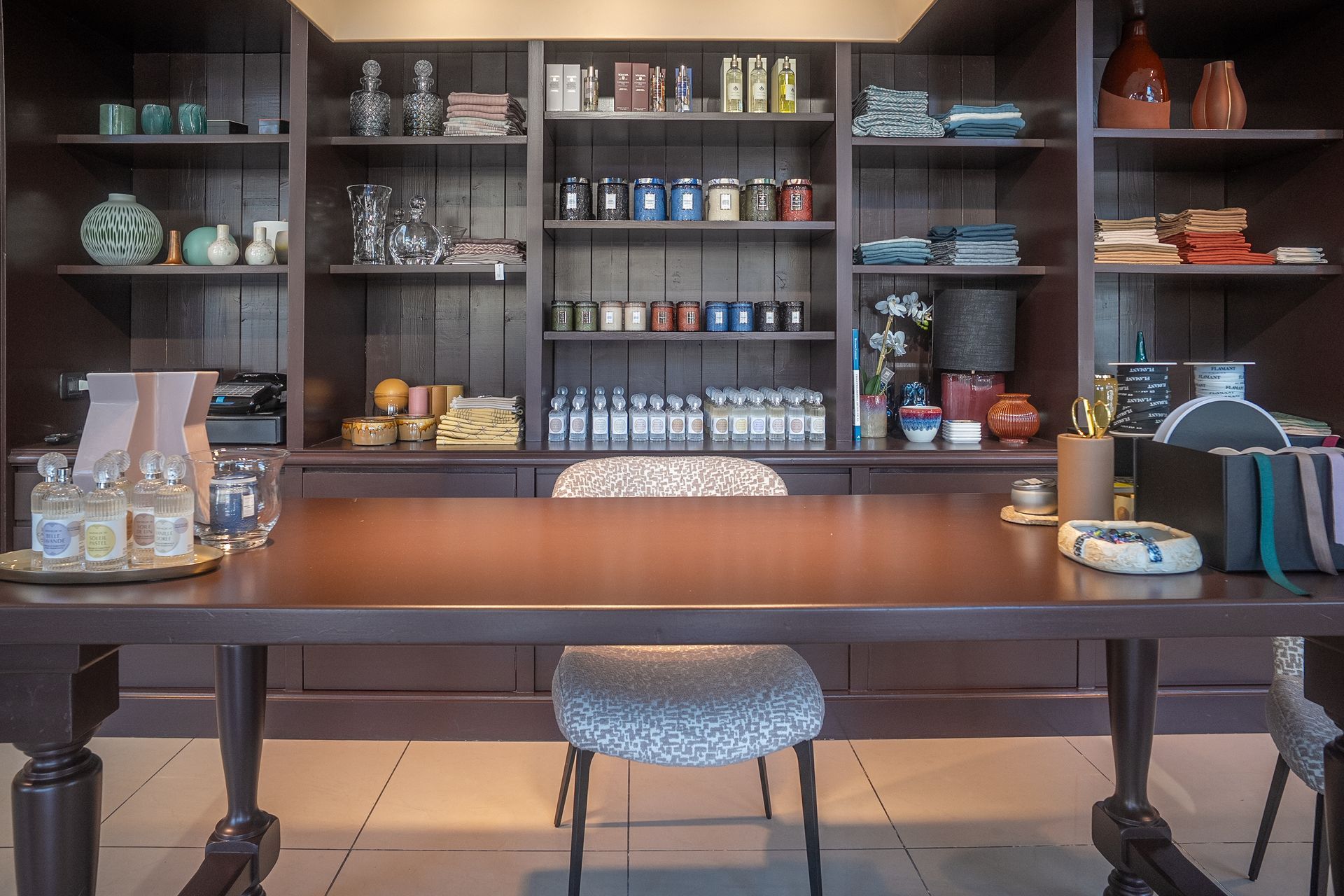 Elegante espositore da bar con scaffali pieni di bottiglie, barattoli e oggetti decorativi dietro un lungo bancone in legno con sgabello.