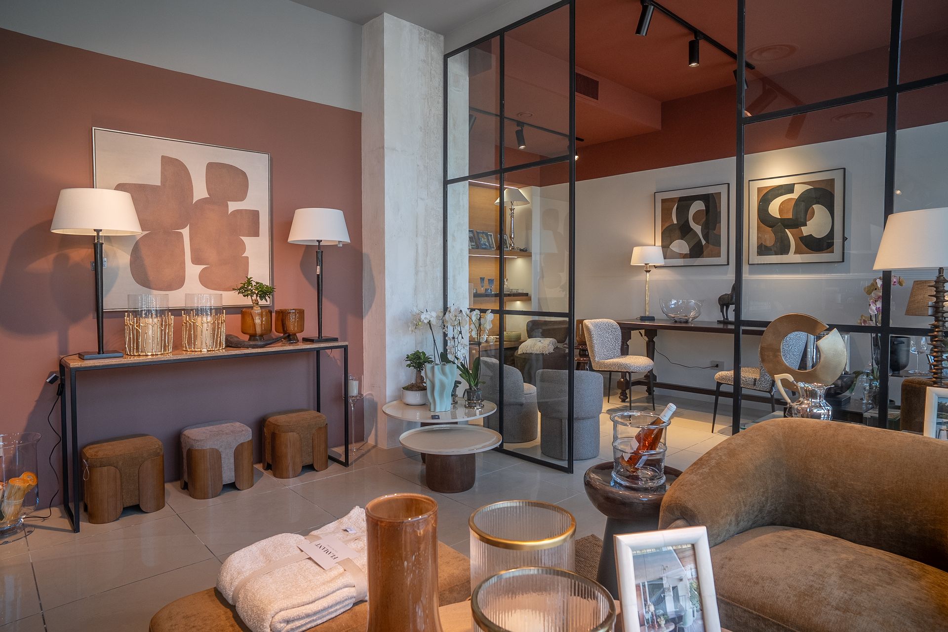 Soggiorno moderno con divano beige, tavolino da caffè in vetro, lampade, consolle e quadri appesi alla parete.