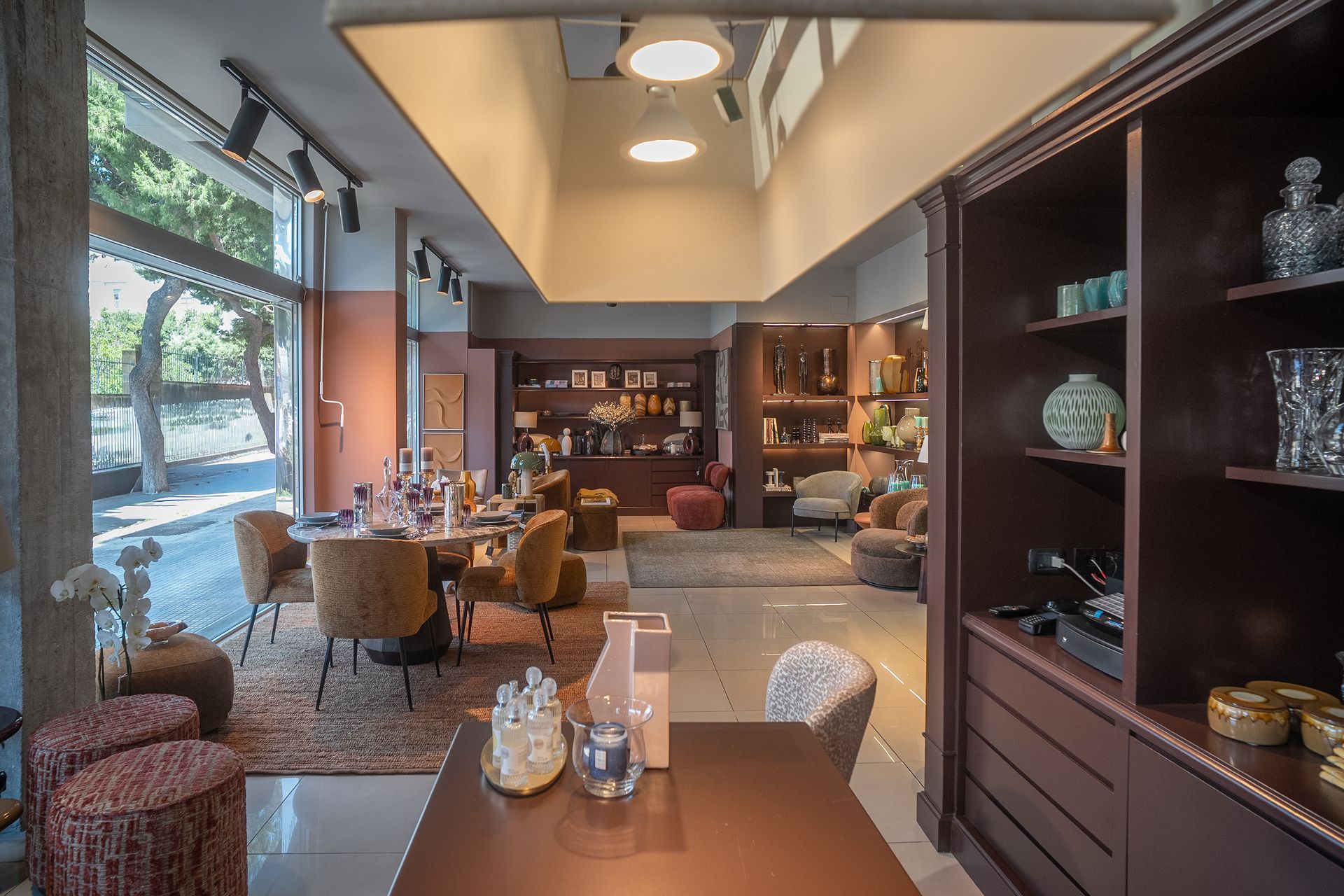Caffè moderno con luci calde, tavoli, scaffali e grandi finestre lungo la parete sinistra.