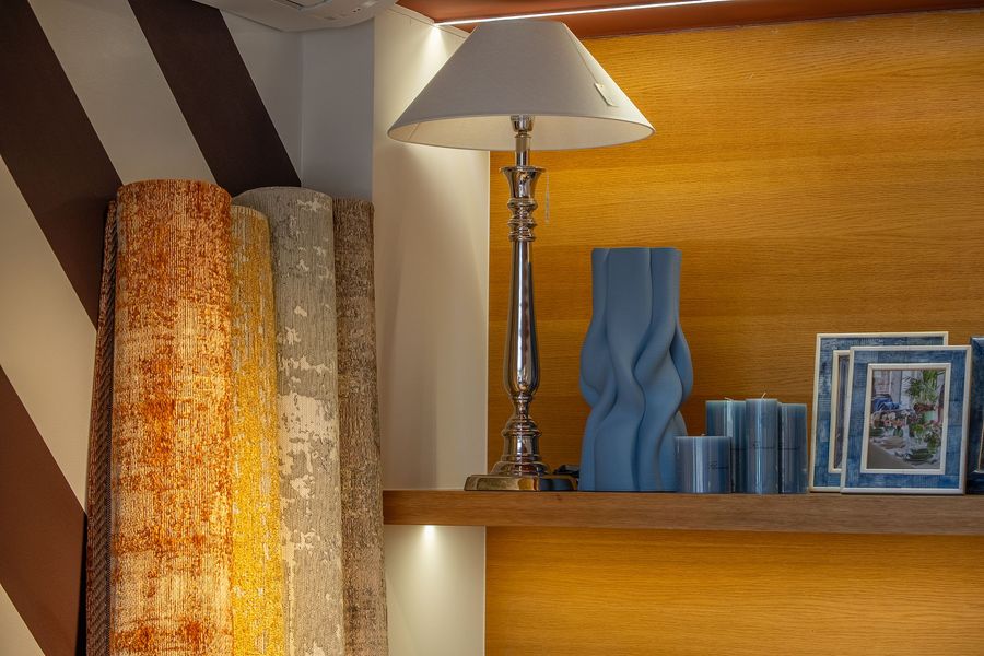 Mensola in legno con lampada, vaso blu, asciugamani piegati e foto incorniciate accanto a tende con trama particolare.