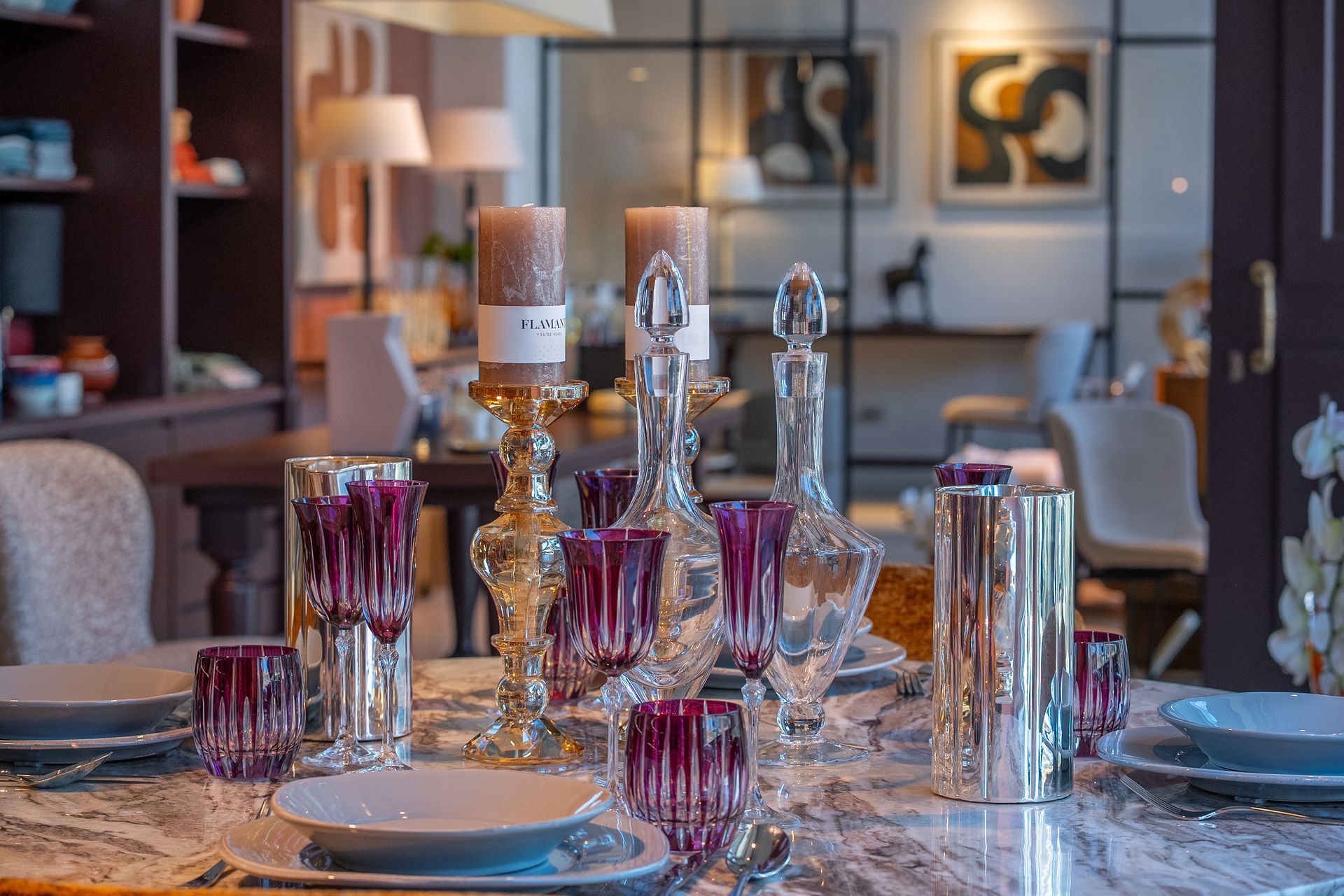 Elegante tavolo da pranzo con bicchieri viola e centrotavola con candele in una stanza moderna illuminata da luci soffuse.