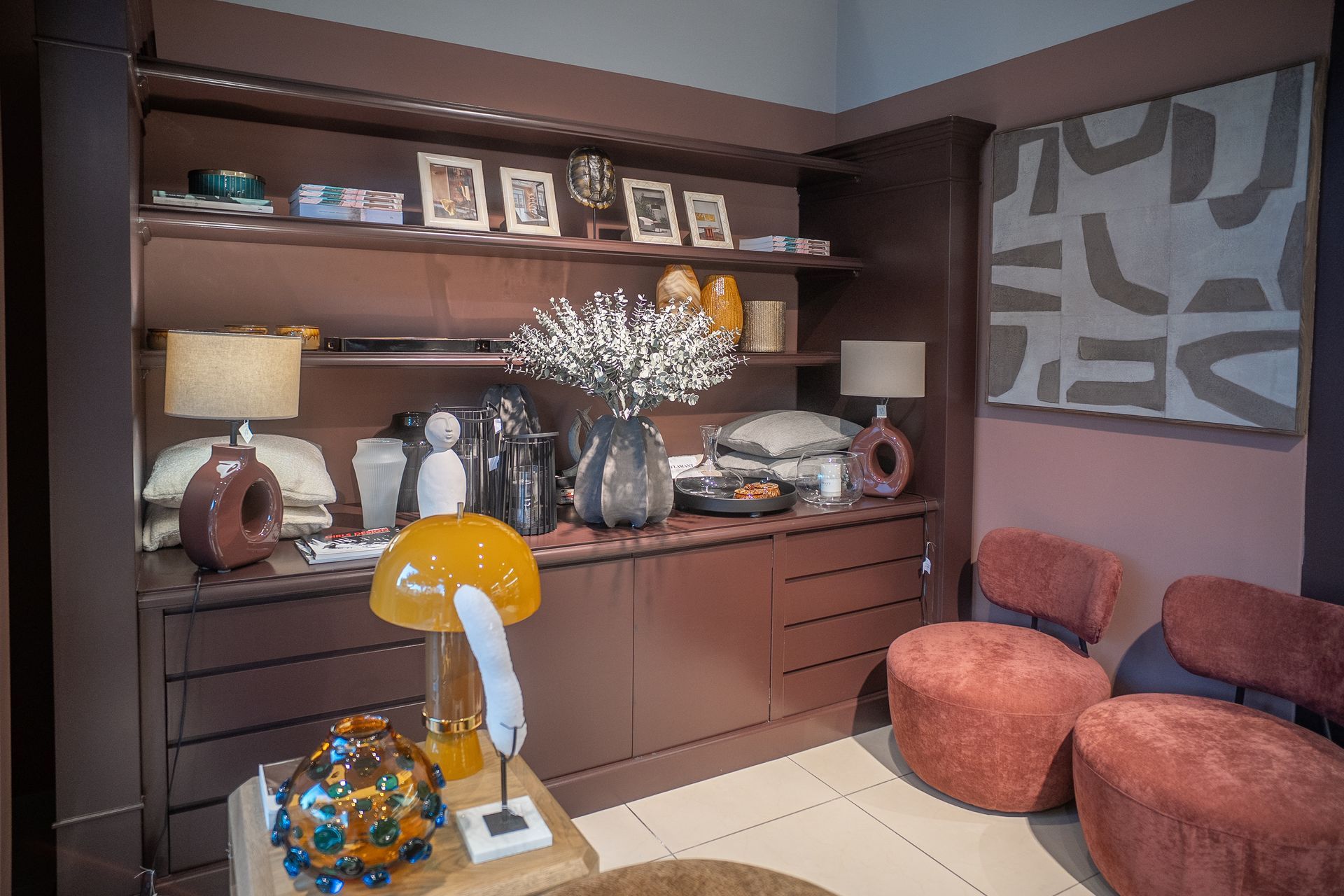 Elegante angolo soggiorno con mensole a muro, foto incorniciate, lampada, oggetti decorativi e sedute arancioni.