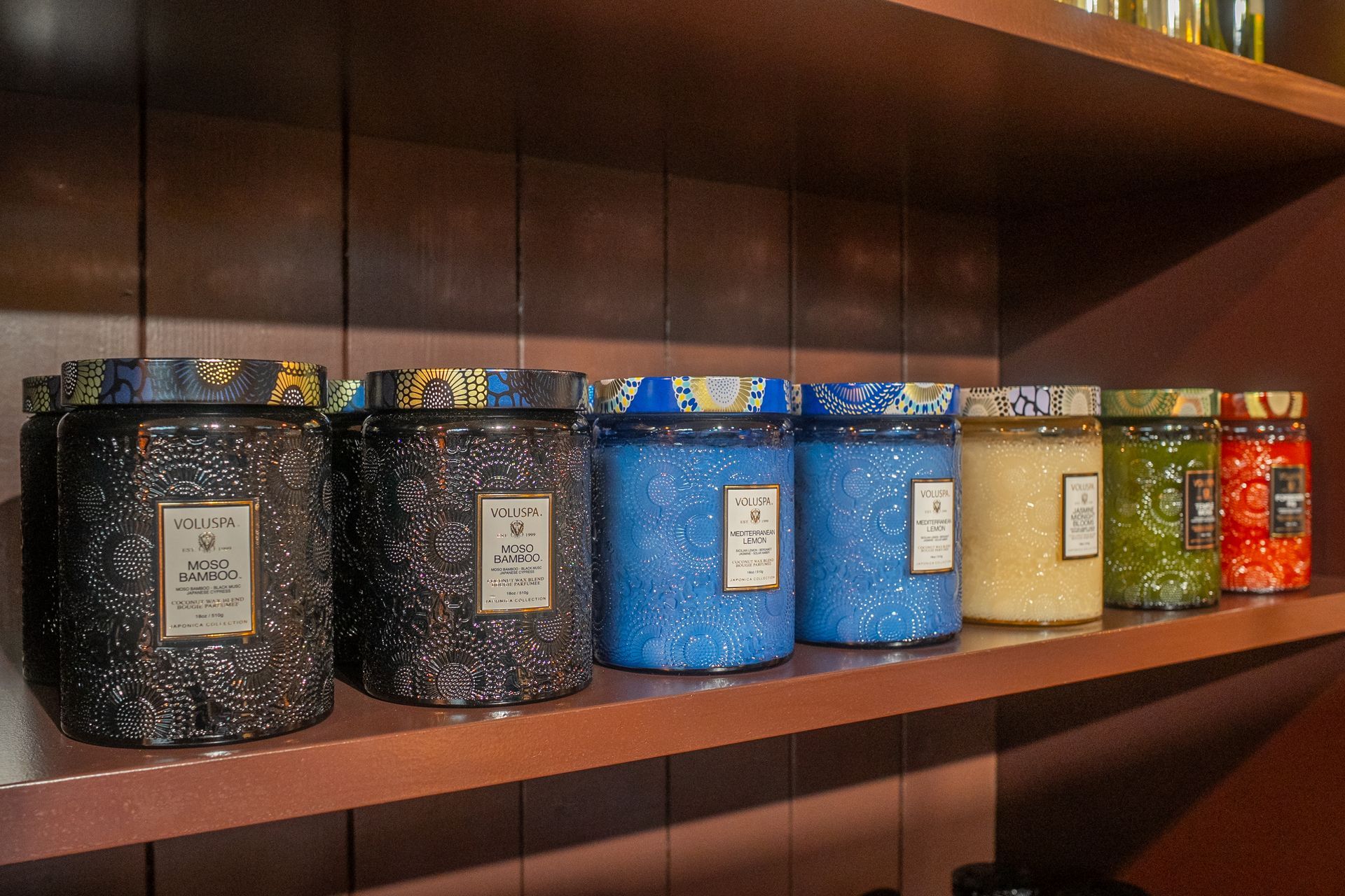 Barattoli decorativi colorati con etichette, allineati su scaffali di legno in una vetrina.