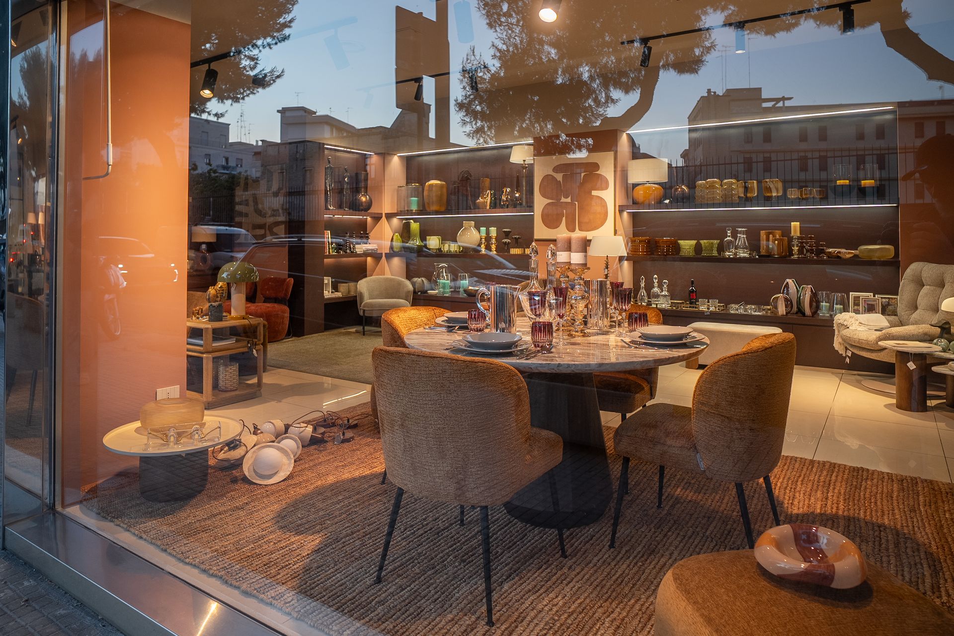 Accogliente interno di un ristorante moderno con sedie intrecciate, tavoli rotondi, luci calde e vetrate a tutta altezza.
