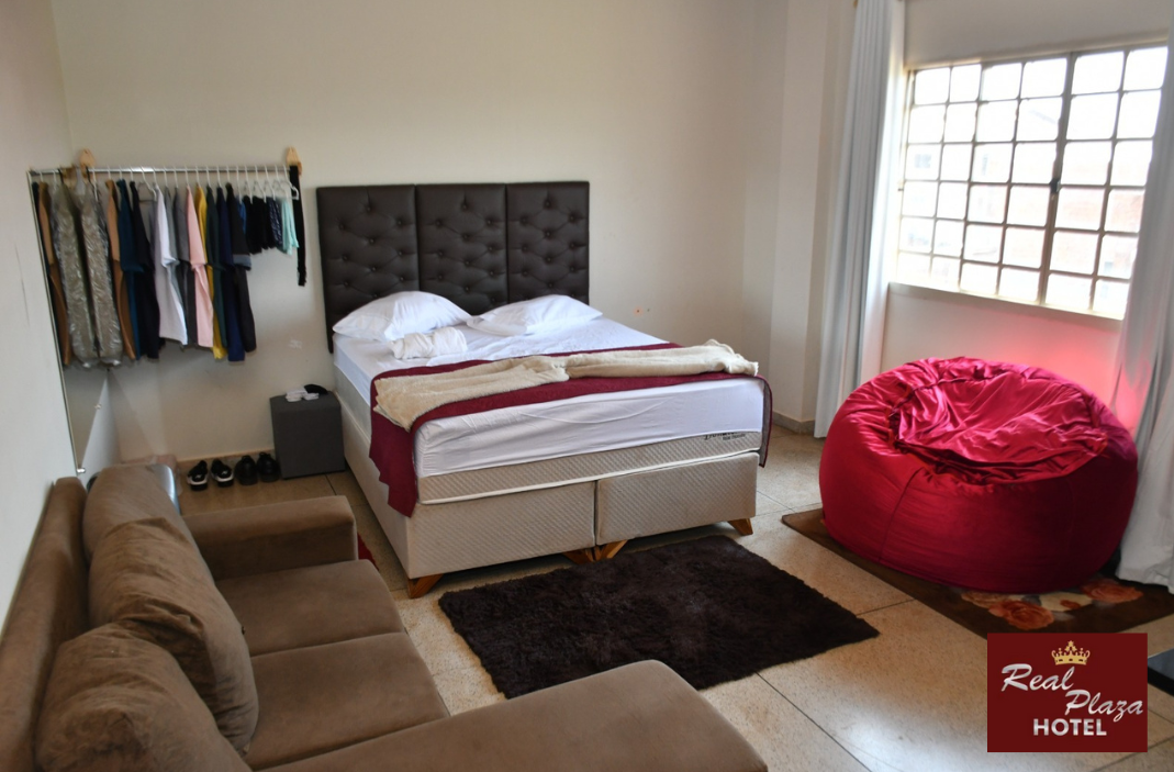 Um quarto de hotel com uma cama, sofá, pufe e janela.
