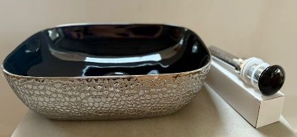 Lavabo de vasija con diseño de mosaico negro y plateado, con desagüe y herrajes sobre un fondo blanco.