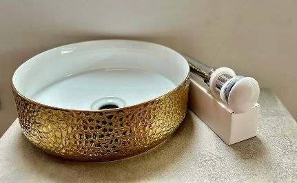 Lavabo de cerámica redondo con textura dorada y interior blanco, conjunto de desagüe sobre bloque blanco,