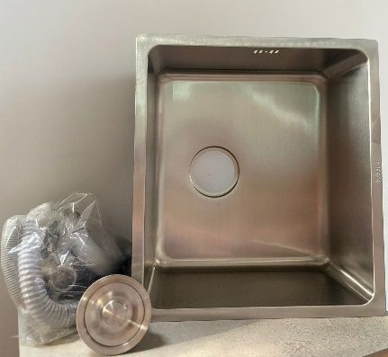 Fregadero de cocina de acero inoxidable con desagüe y plomería sobre superficie clara.